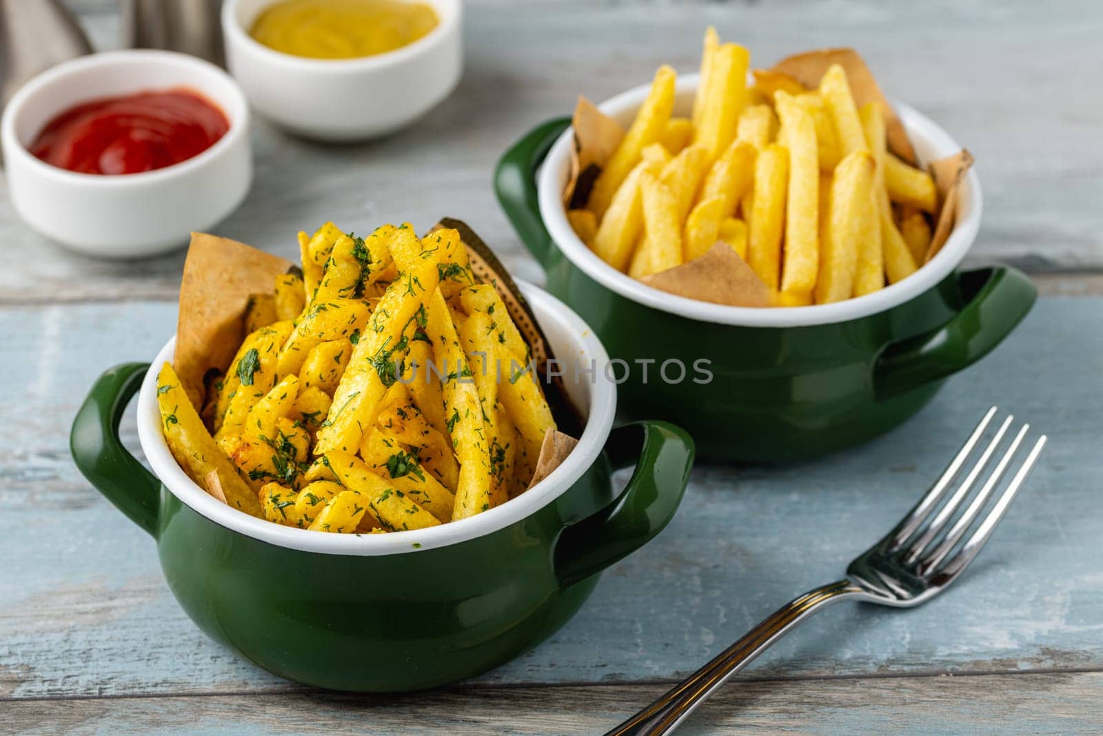 Golden French Fries in an enamel bowl with various sauces on the side