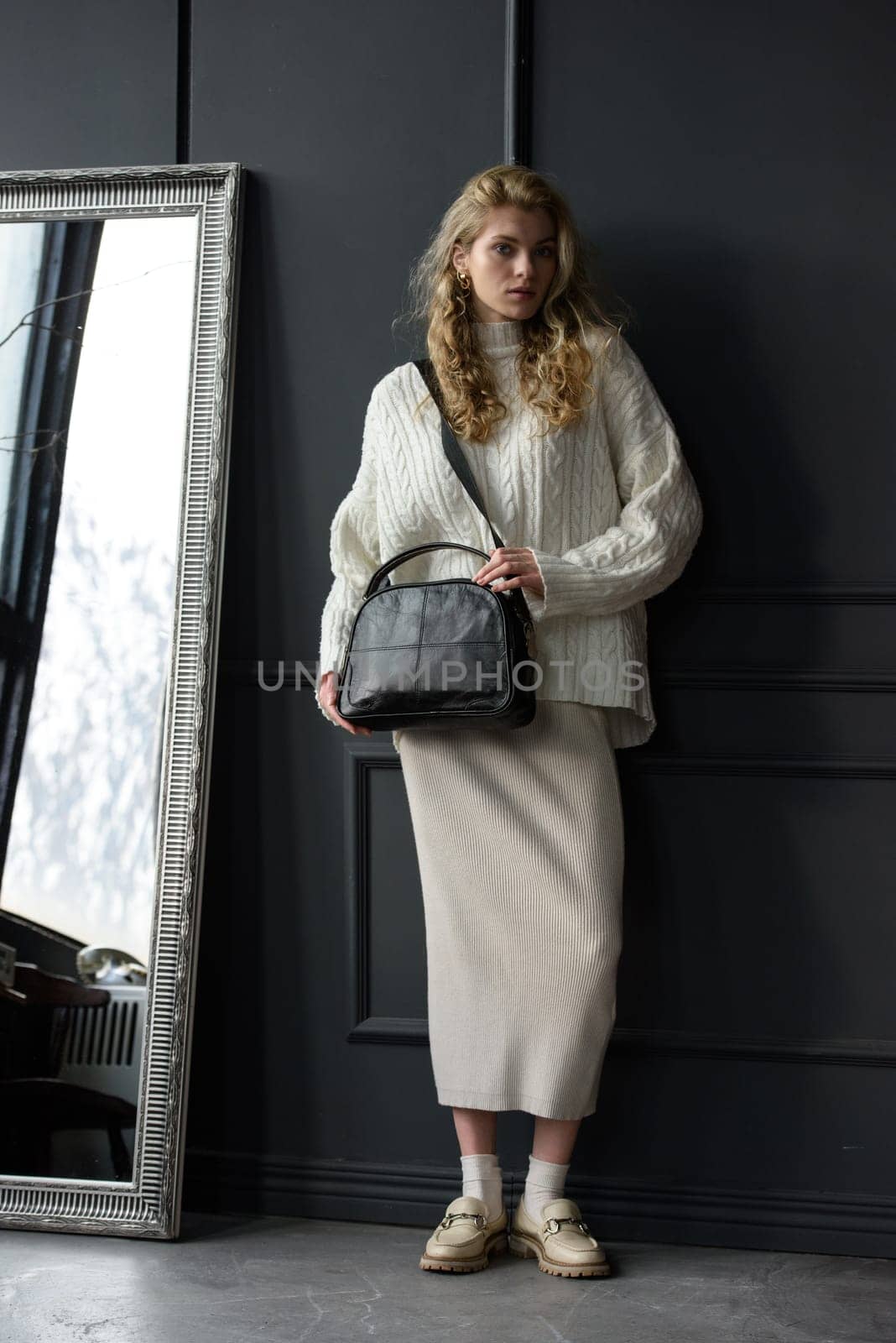 Studio portrait of beautiful woman with a curly blond hair holding black bag, posing on gray background. by Ashtray25