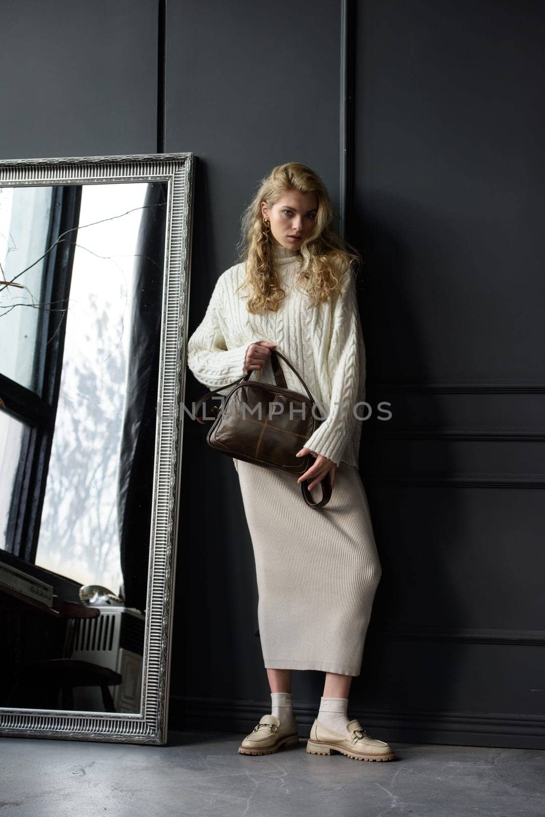 Studio portrait of beautiful woman with a curly blond hair holding brown bag, posing on gray background. by Ashtray25