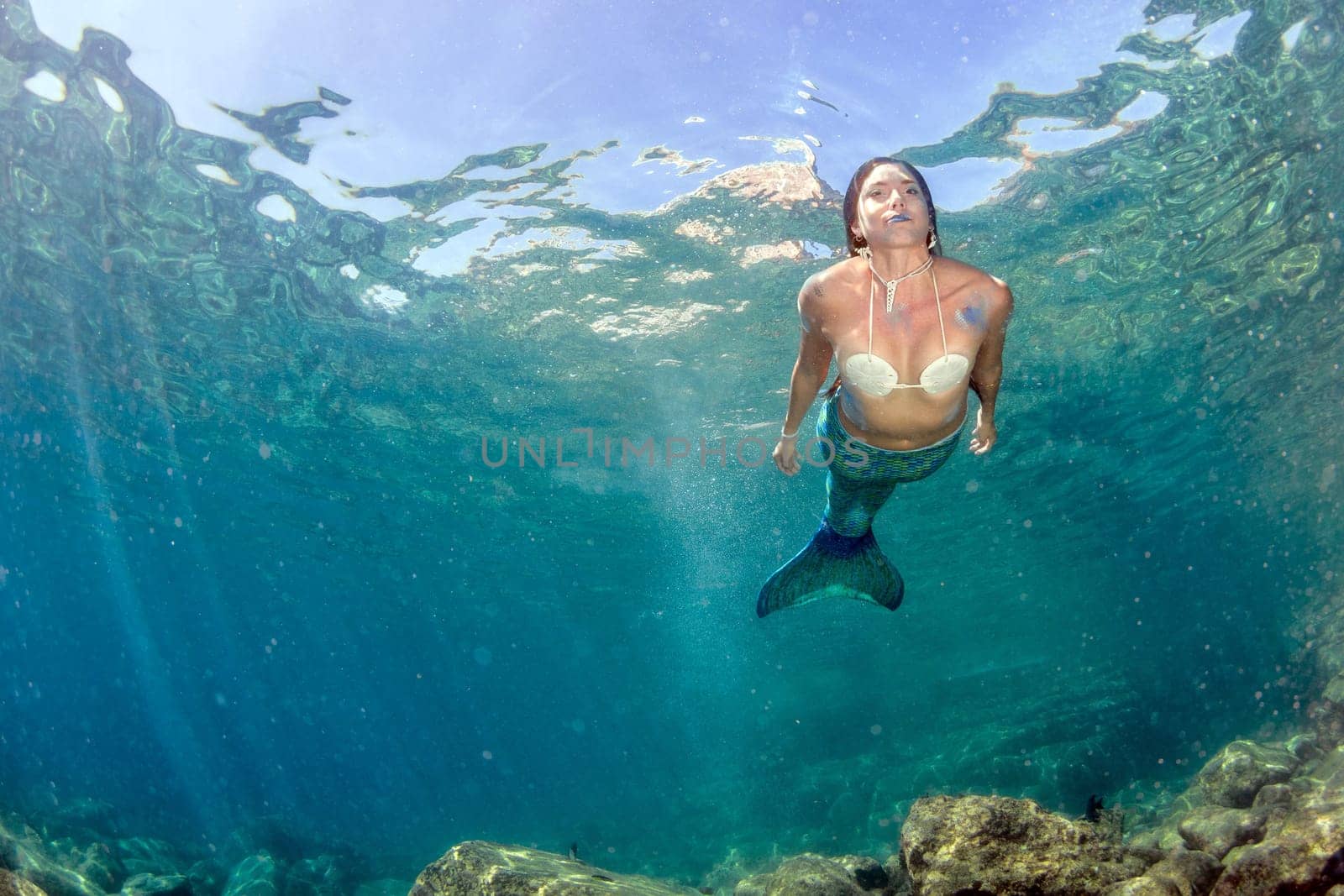 Mermaid swimming underwater in the deep blue sea by AndreaIzzotti