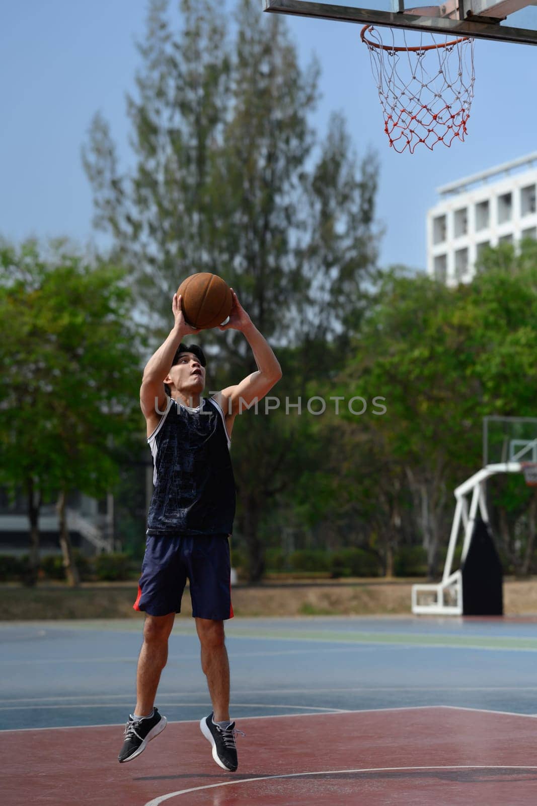 Full length of young sportsman jumping in basketball court and throwing ball to the basket.