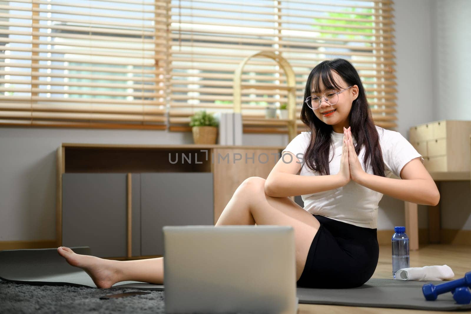 Young Asian woman practice yoga on mat and watching online lessons on laptop.