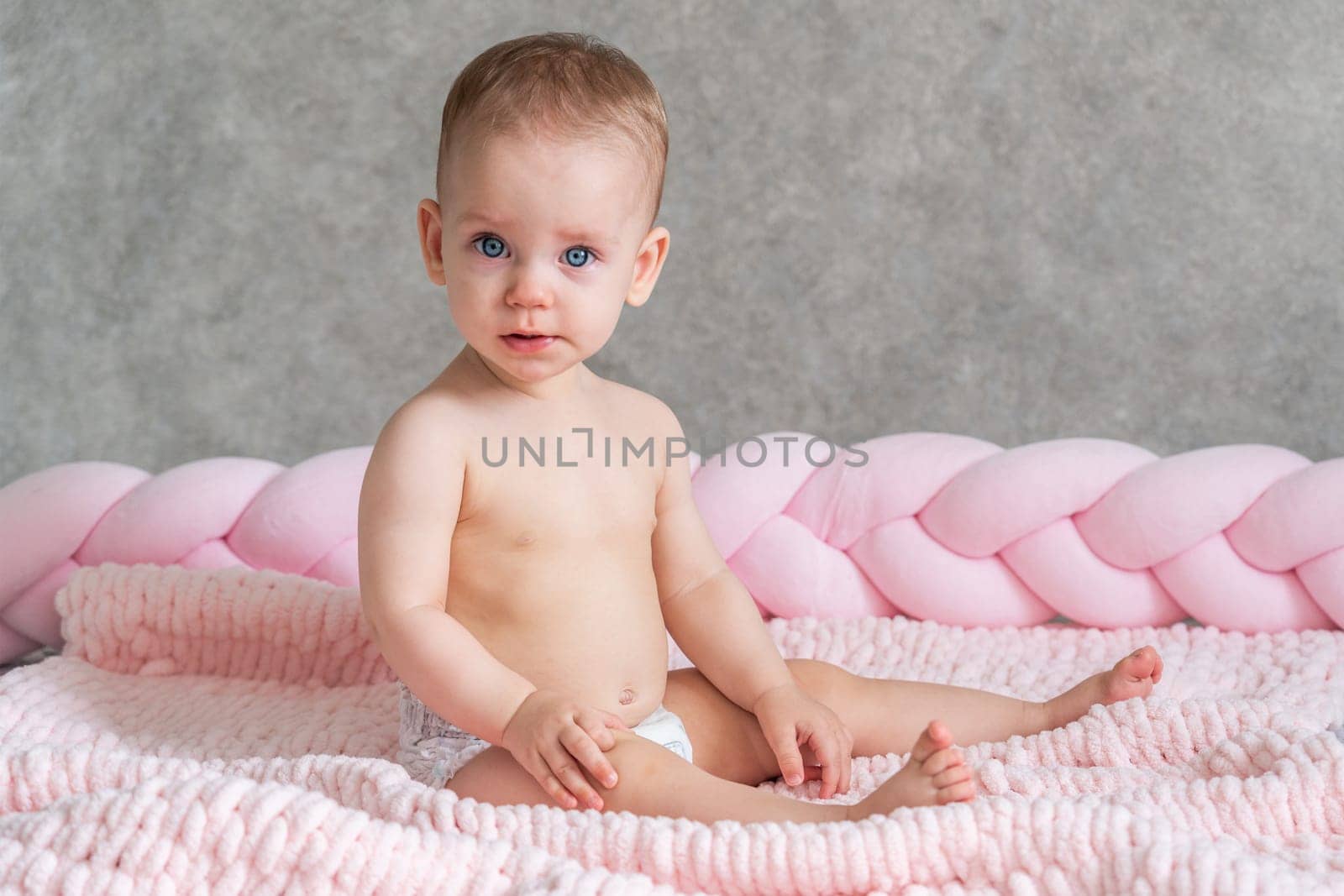 A direct look into the camera of a baby sitting on the bed. Universal concept.