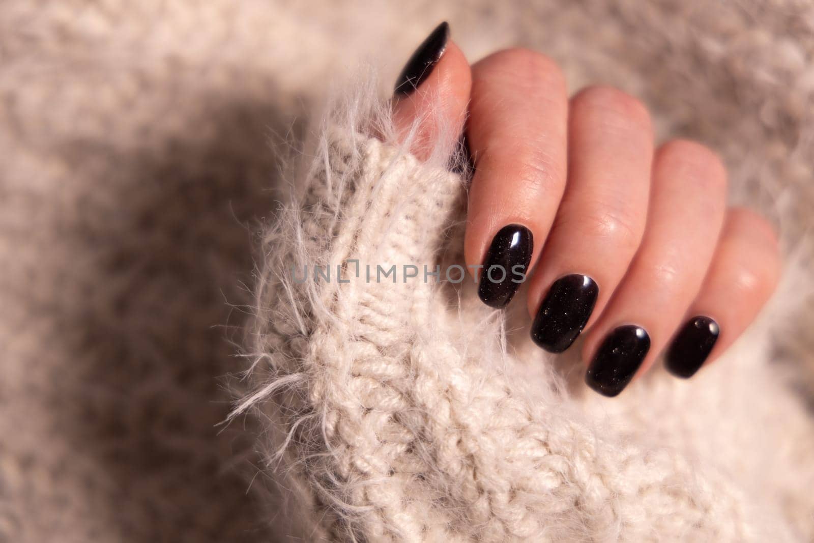 Beautiful female manicure of black color. Woman hand in cashmere knitwear by Ri6ka