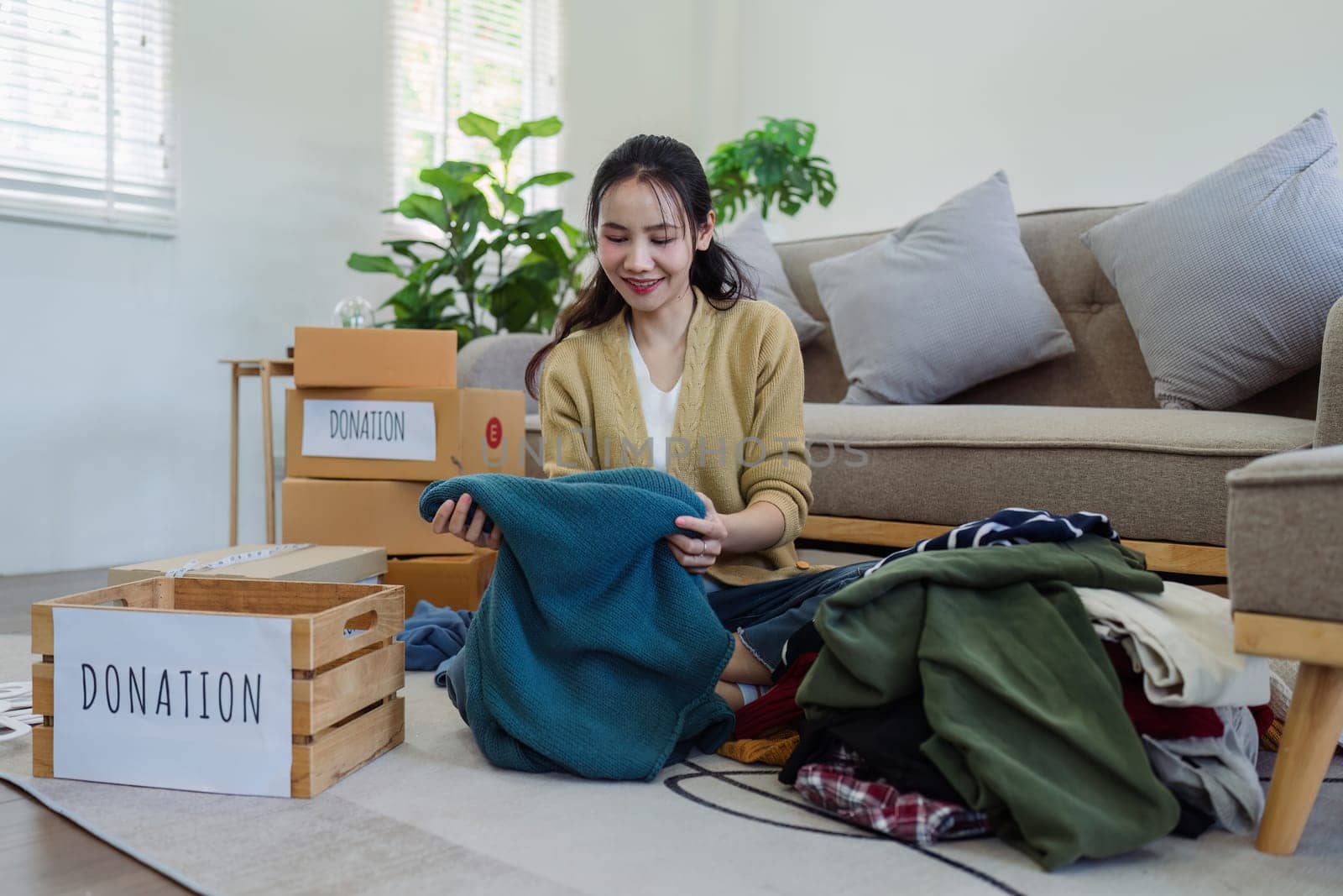 Asian young woman packing clothes at home, putting on stuff into donate box with second hand clothes. Help poor people. Donation concept by itchaznong