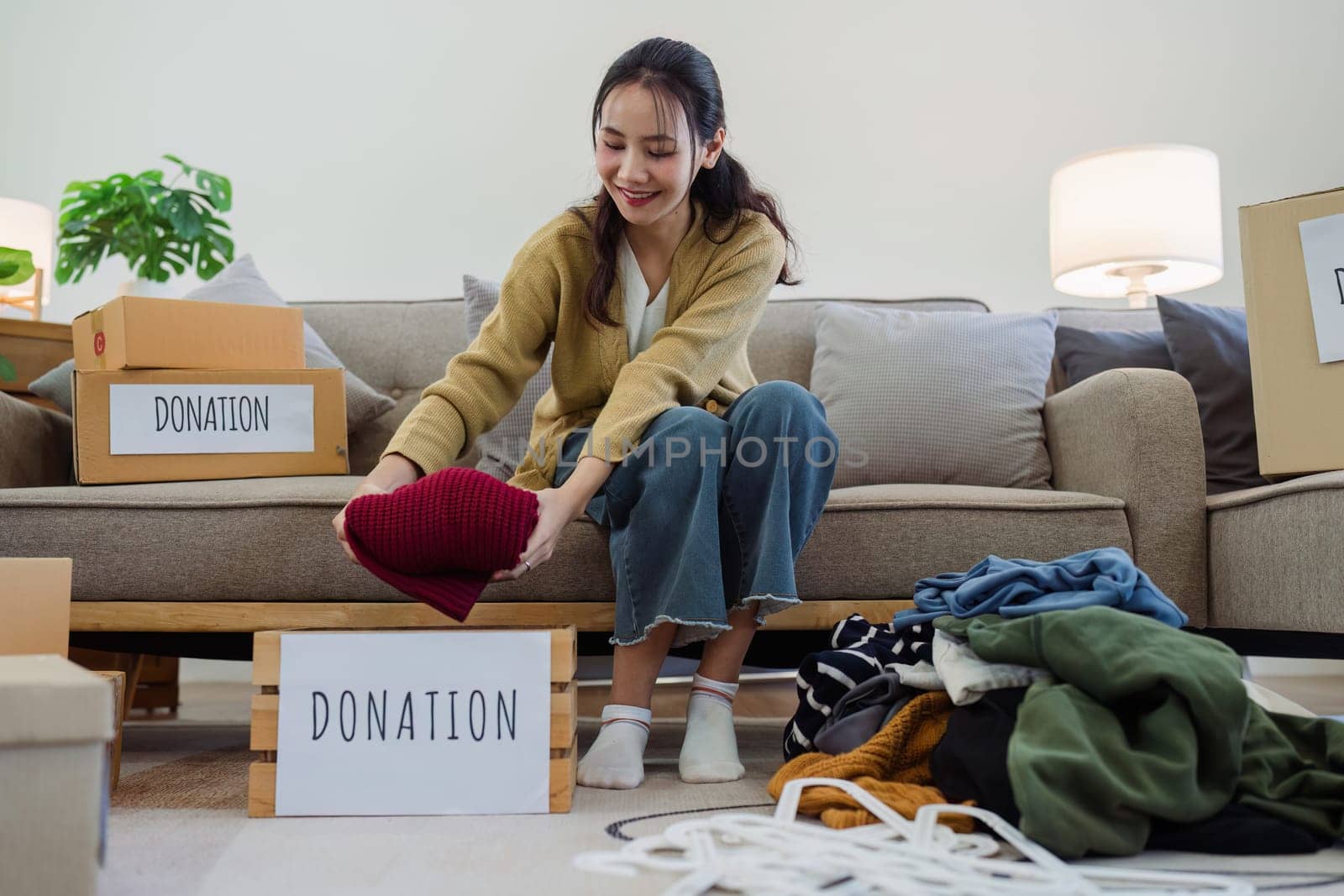 A woman is sorting through a pile of clothes and placing them in donation boxes. She is smiling as she works, indicating that she is happy to be helping others