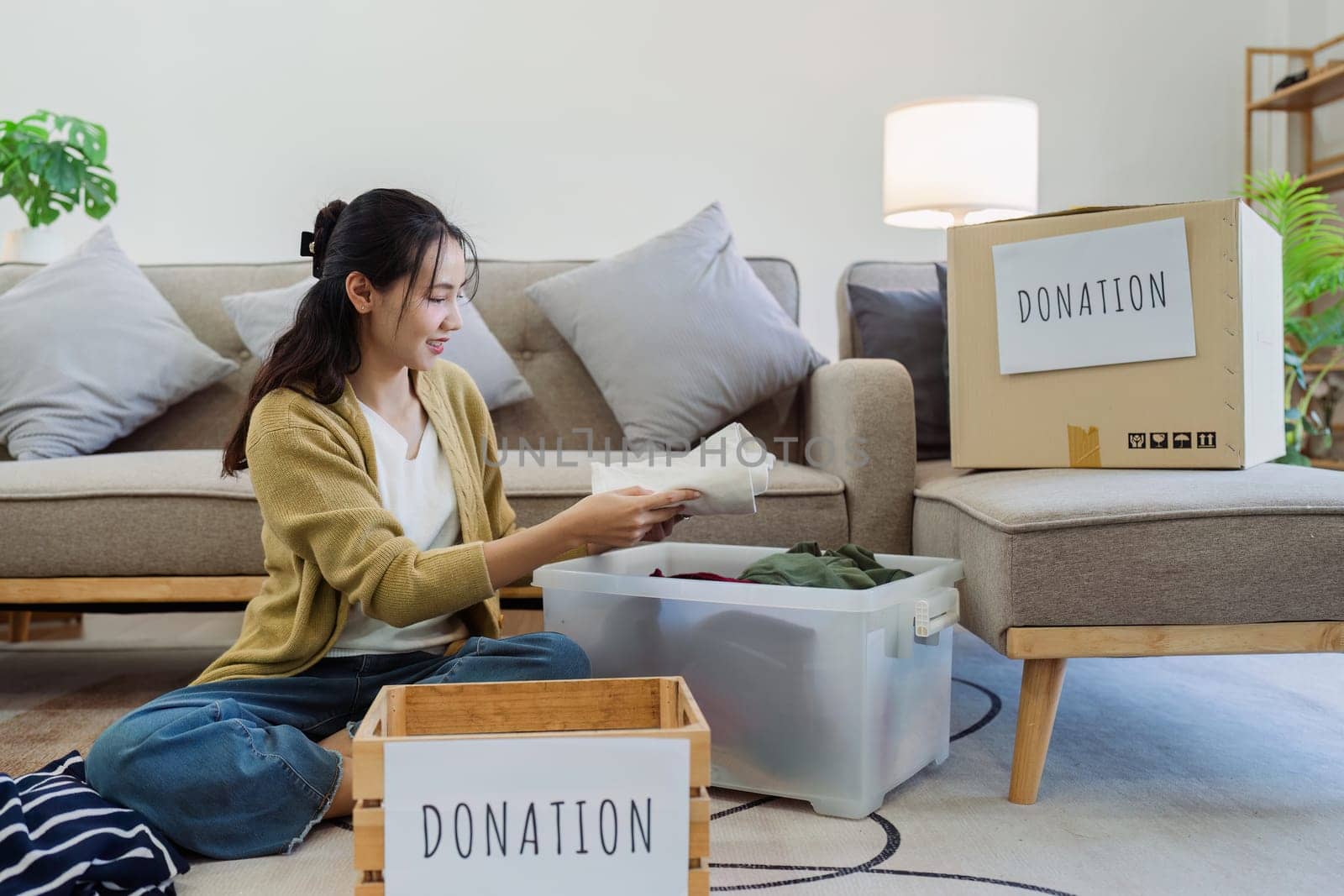 Asian young woman packing clothes at home, putting on stuff into donate box with second hand clothes. Help poor people. Donation concept by itchaznong