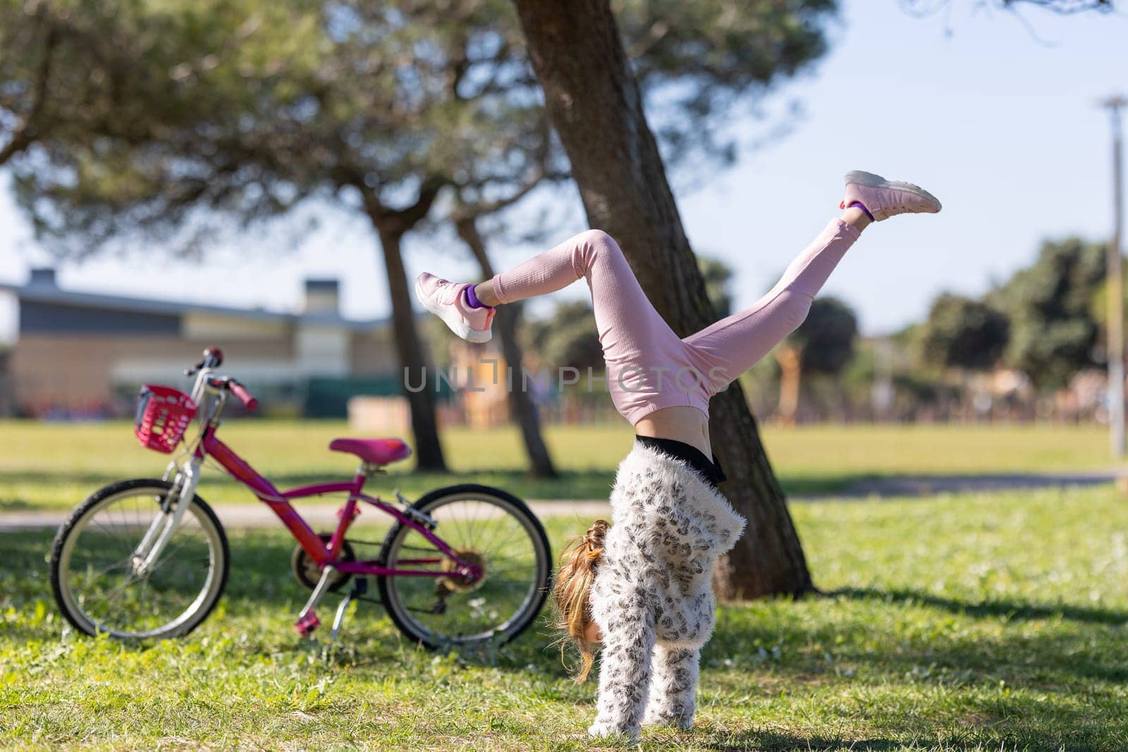 A girl is doing a handstand in the grass next to a bicycle by Studia72