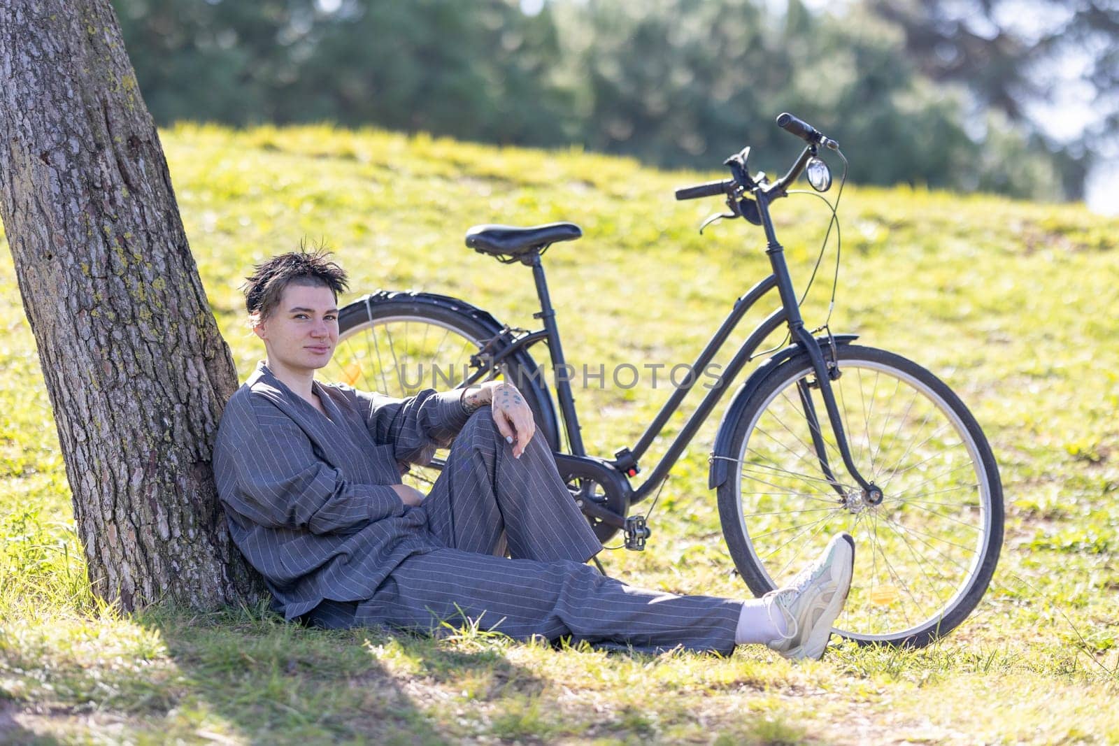 A woman is sitting on the grass next to a bicycle. He is wearing a black shirt and pants