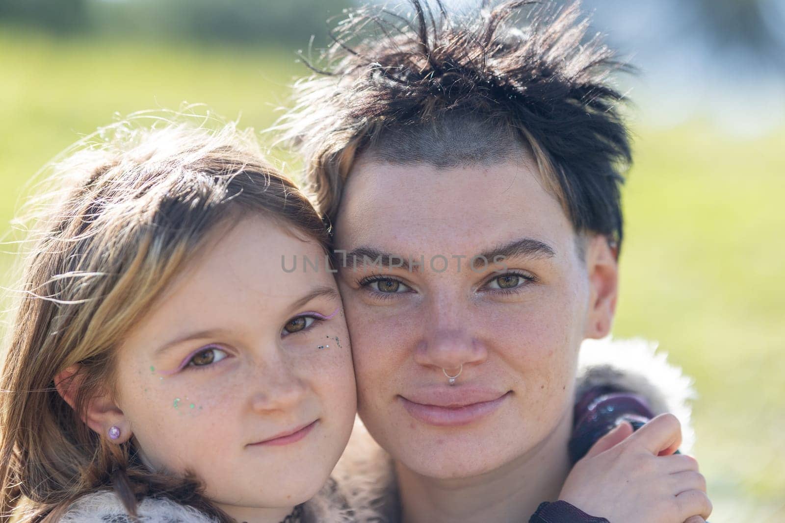 A woman with a shaved head and a girl with long hair are posing for a picture. The girl has a nose ring and the woman has a nose piercing