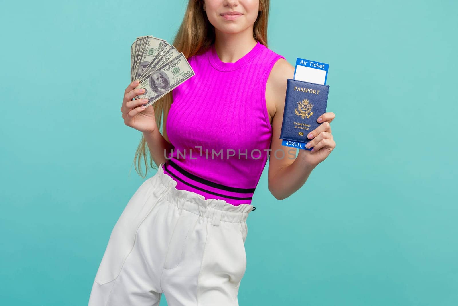 Studio portrait of pretty young student woman holding passport with tickets and money. Isolated on bright blue background.