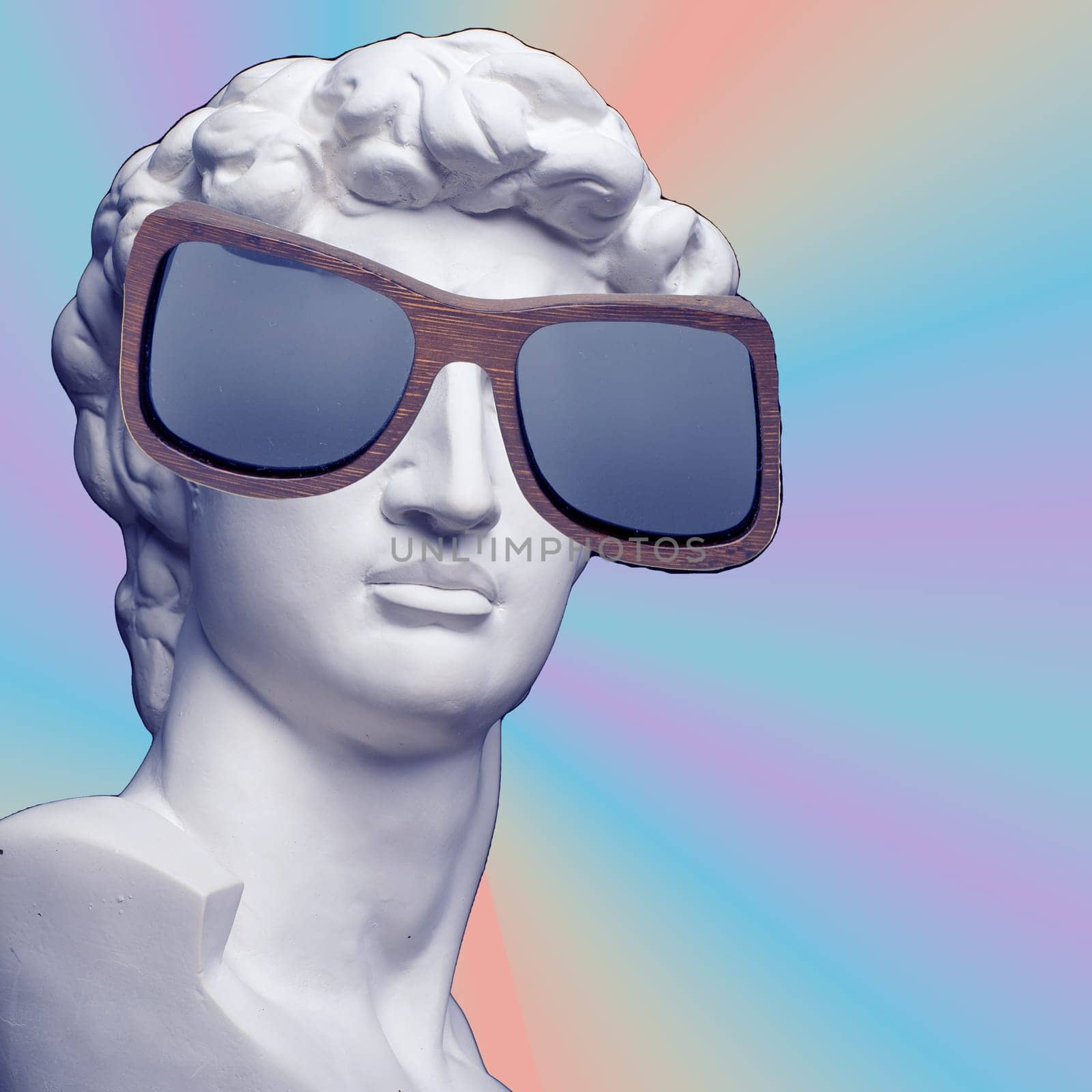 Collage of contemporary art. Concept. Gypsum head of David in sunglasses on rainbow background