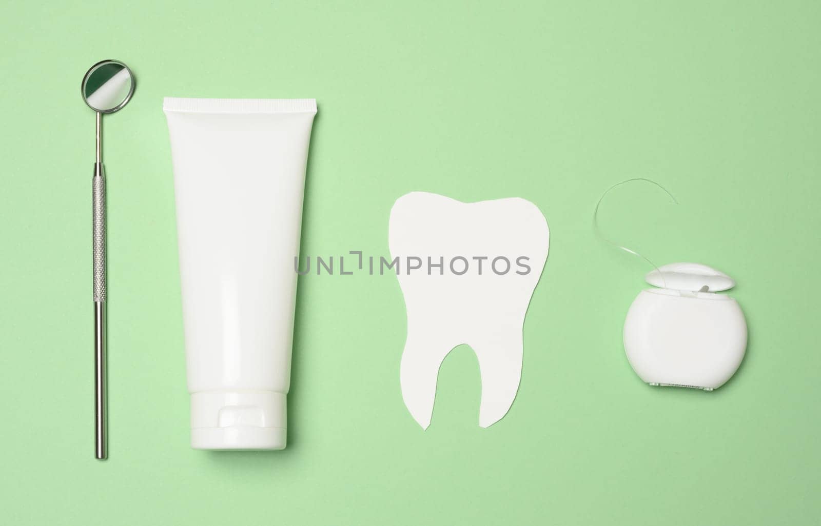 Dental mirror, tube of toothpaste and dental floss on a green background by ndanko