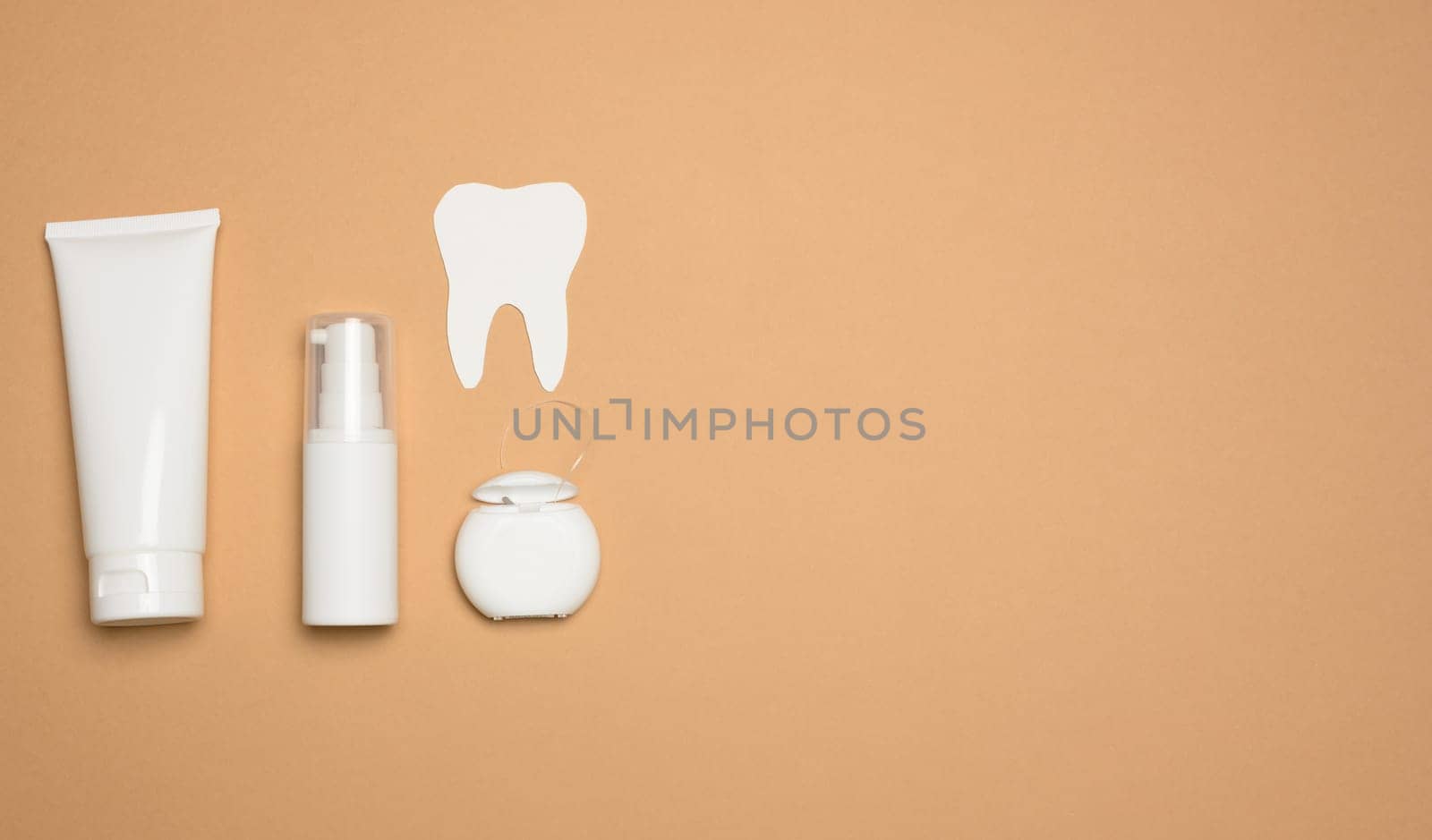 Tube with toothpaste, dental floss  on a brown background, oral hygiene. Copy space

