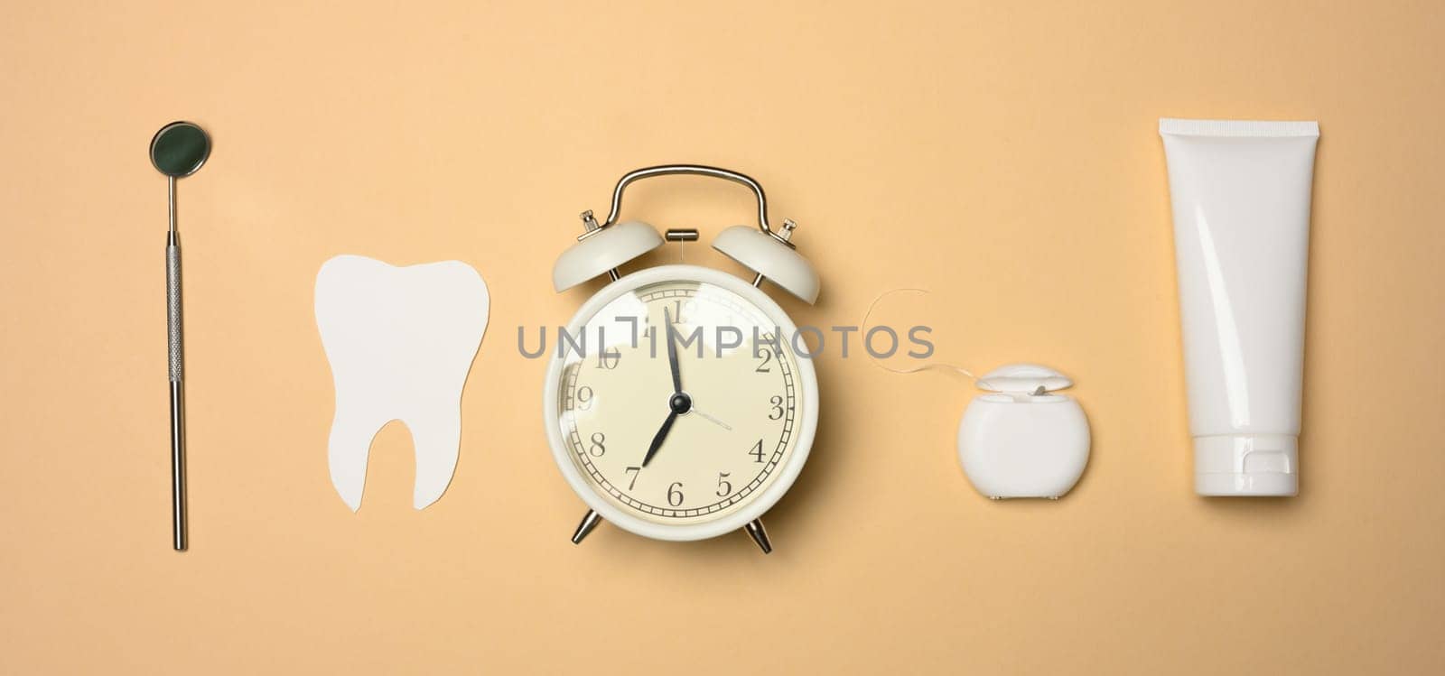Alarm clock, tube of toothpaste and paper tooth on brown background, oral hygiene care, top view