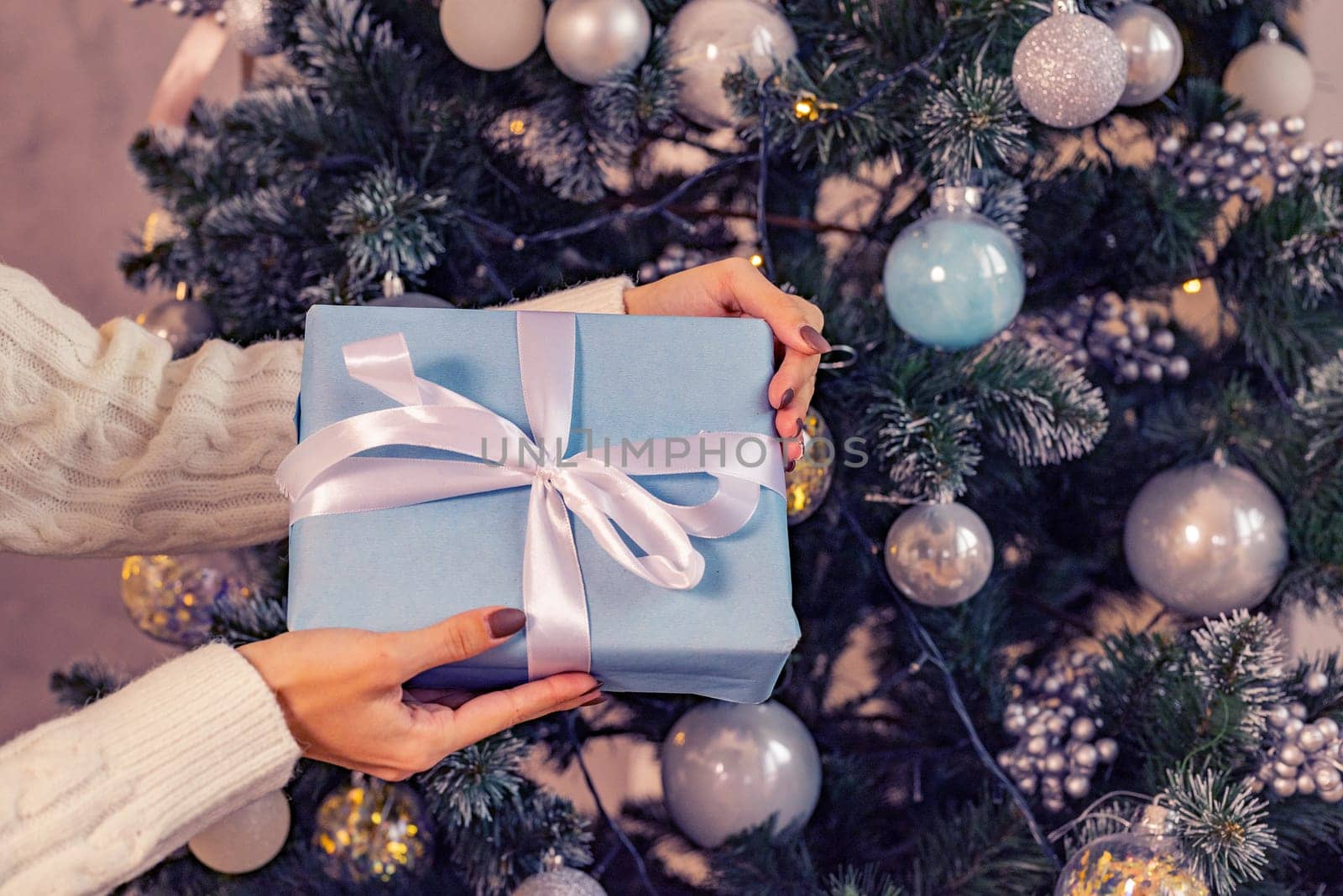 A gift in the hands woman against the backdrop of the lights of the Christmas tree