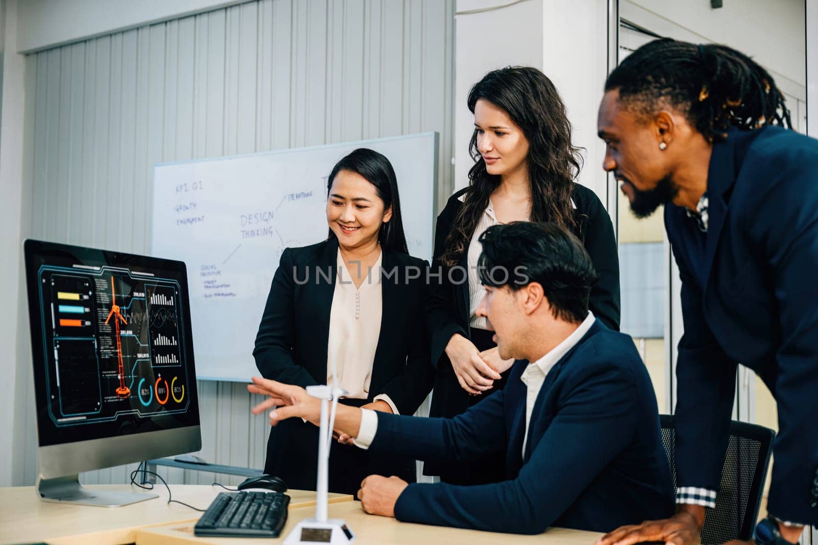 A team of professionals gathers around a desktop computer, engaging in discussion and brainstorming. Their diverse perspectives promote cooperation, teamwork, and successful marketing planning.