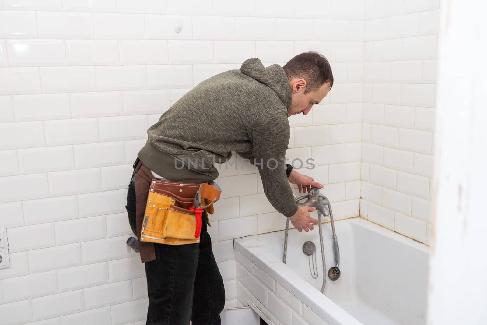 A male plumber with wrench repairs the faucet in the bathroom. replacement and maintenance of plumbing. handyman service. small business. High quality photo