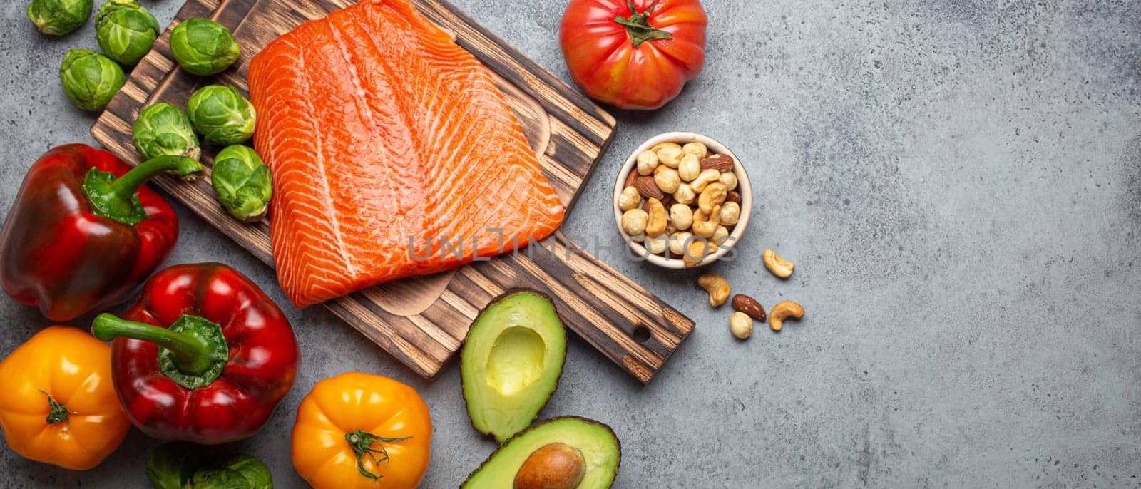 Fresh raw salmon fillet on wooden cutting board, organic bio vegetables and nuts, rustic stone grey background top view. Ingredients full of vitamins for healthy diet and nutrition, space for text by its_al_dente