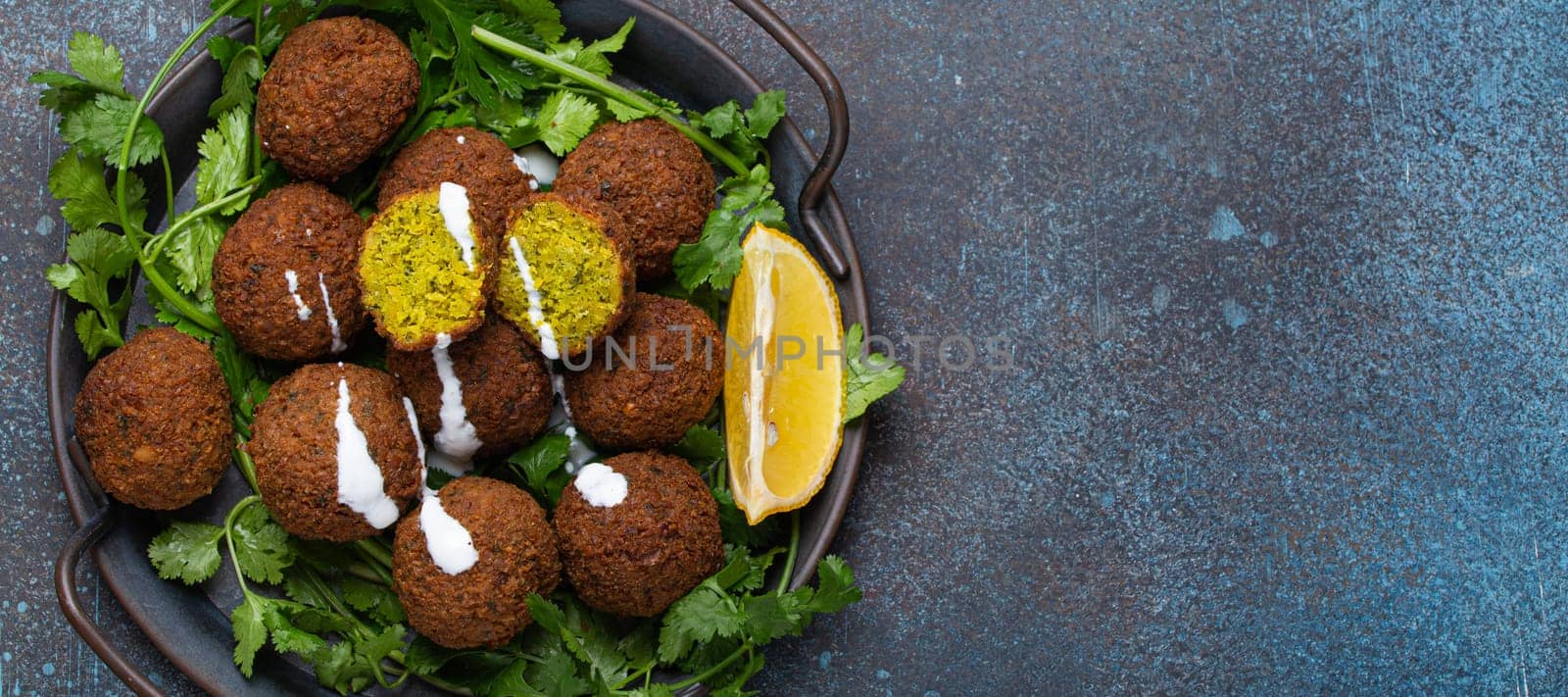 Plate of fried falafel balls served with fresh green cilantro and lemon top view on rustic concrete background. Traditional vegan dish of Middle Eastern cuisine, copy space by its_al_dente