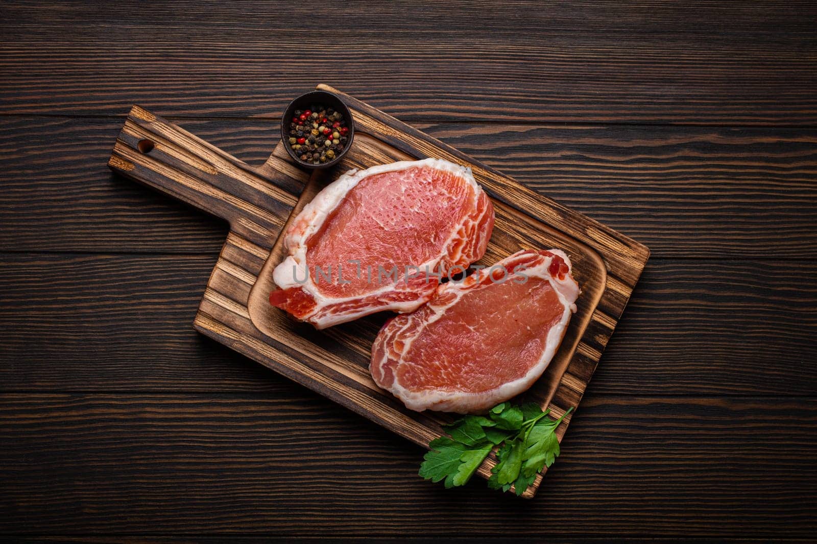 Cut raw meat pork steaks with seasonings on kitchen cutting board, rustic wooden background from above, ready for BBQ. Pork loin chops by its_al_dente