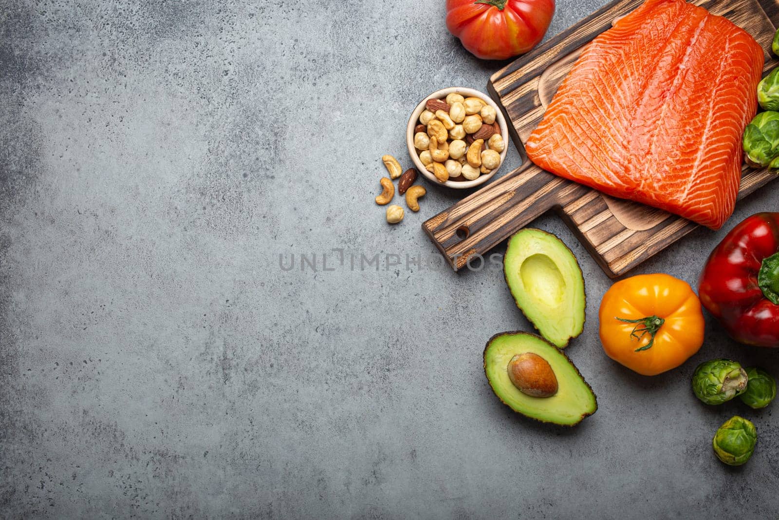 Fresh raw salmon fillet on wooden cutting board, organic bio vegetables and nuts on rustic stone grey background top view. Ingredients full of vitamins for healthy diet and nutrition, space for text
