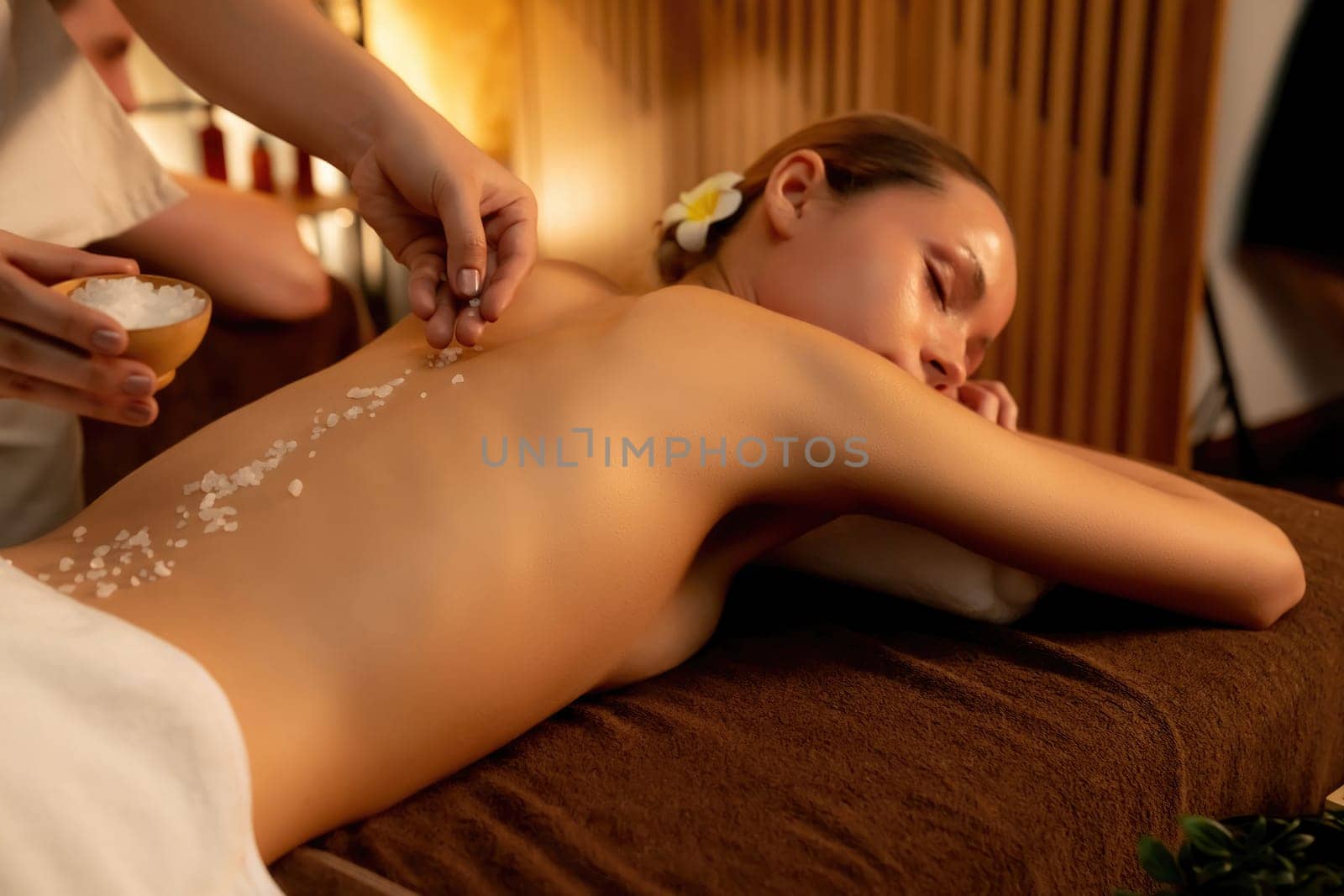 Couple customer having exfoliation treatment in luxury spa salon with warmth candle light ambient. Salt scrub beauty treatment in Health spa body scrub. Quiescent