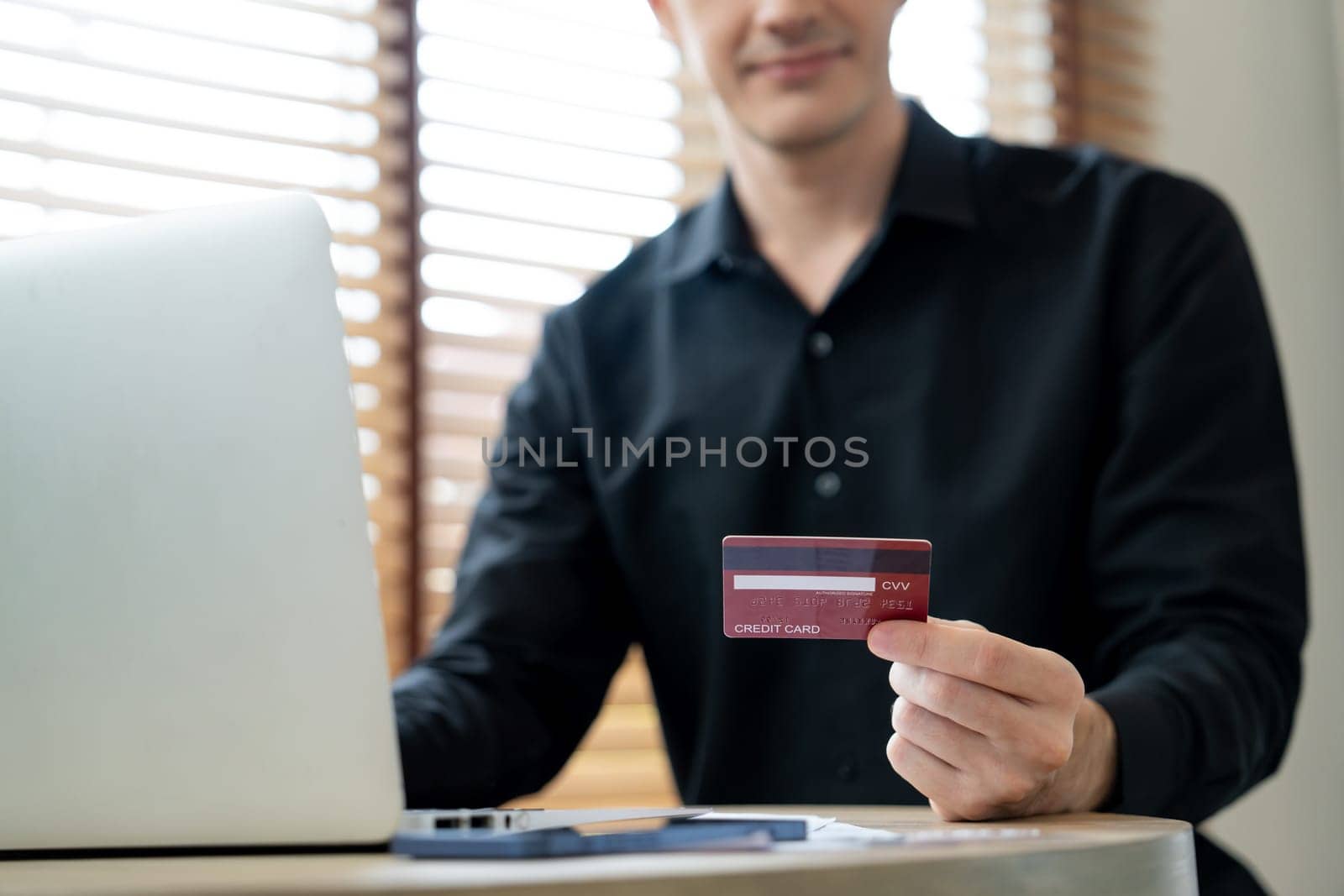 Young man using laptop with credit card for internet banking, online shopping E commerce by online payment gateway at home office. Modern and convenience online purchasing with debit card. Unveiling