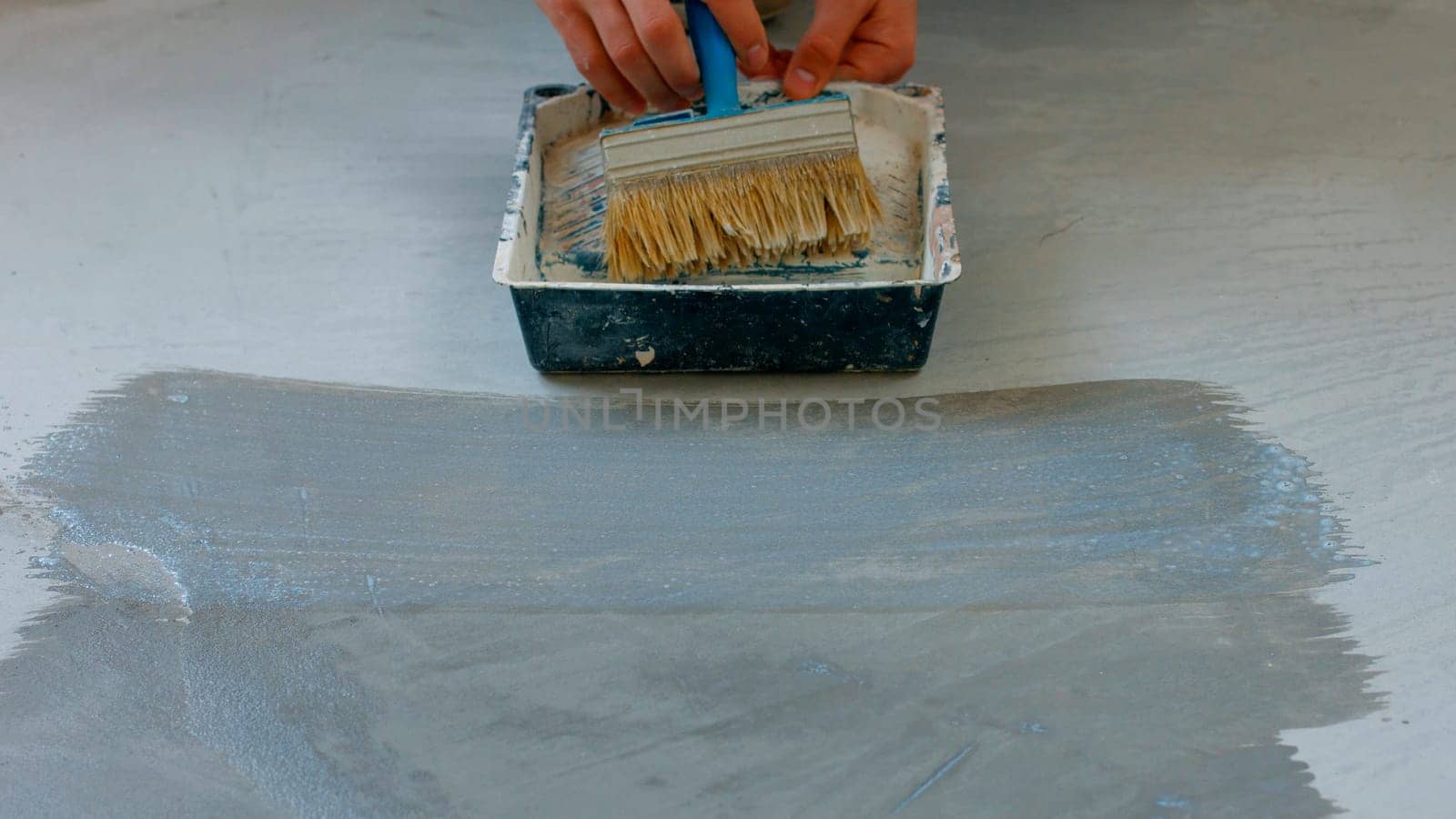 House painter primer concrete floor. Worker preparing the floor under painting.