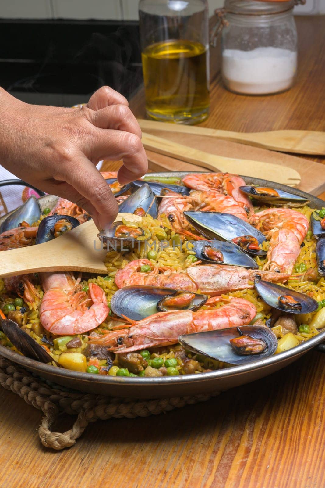 Hand gently stirring a seafood paella with shrimp and mussels using a wooden spatula, typical Spanish cuisine, Majorca, Balearic Islands, Spain,