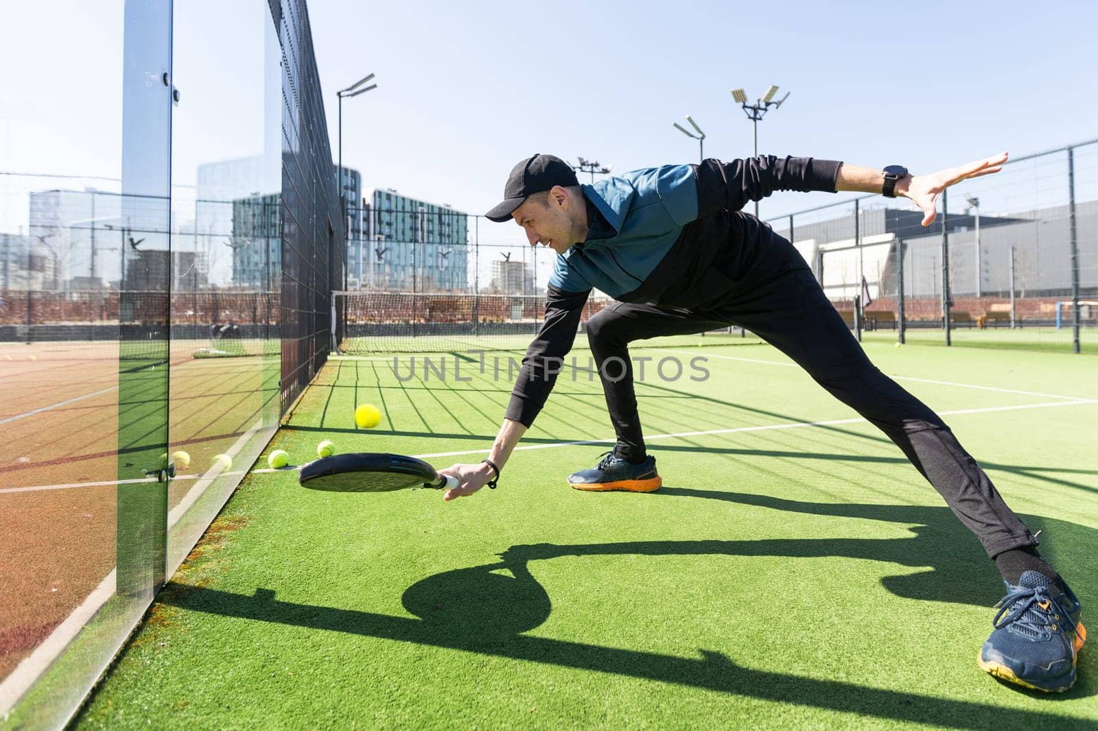 A padel player jump to the ball, good looking for posts and poster. Man with black racket playing a match in the open behind the net court outdoors. Professional sport concept with space for text. High quality photo