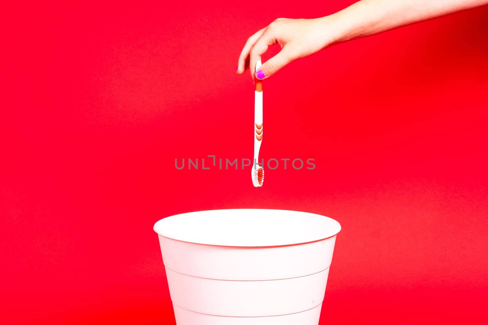 The toothbrush is thrown into a trash basket. Red background, copy space.