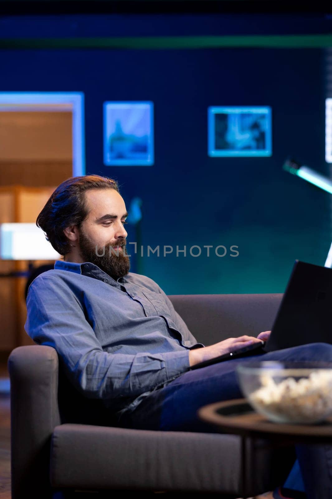 Man enjoying popcorn while watching TV and scrolling on social media on laptop by DCStudio