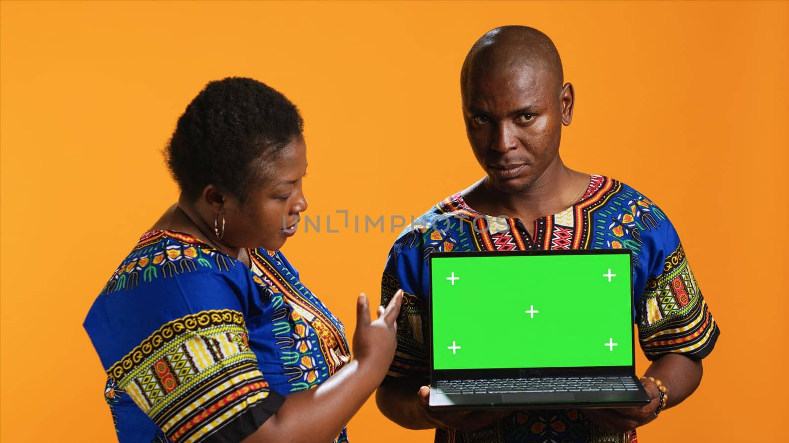 Ethnic couple pointing at laptop with greenscreen display, posing in studio with portable pc presenting isolated copyspace layout. Man and woman looking at blank mockup template on camera.