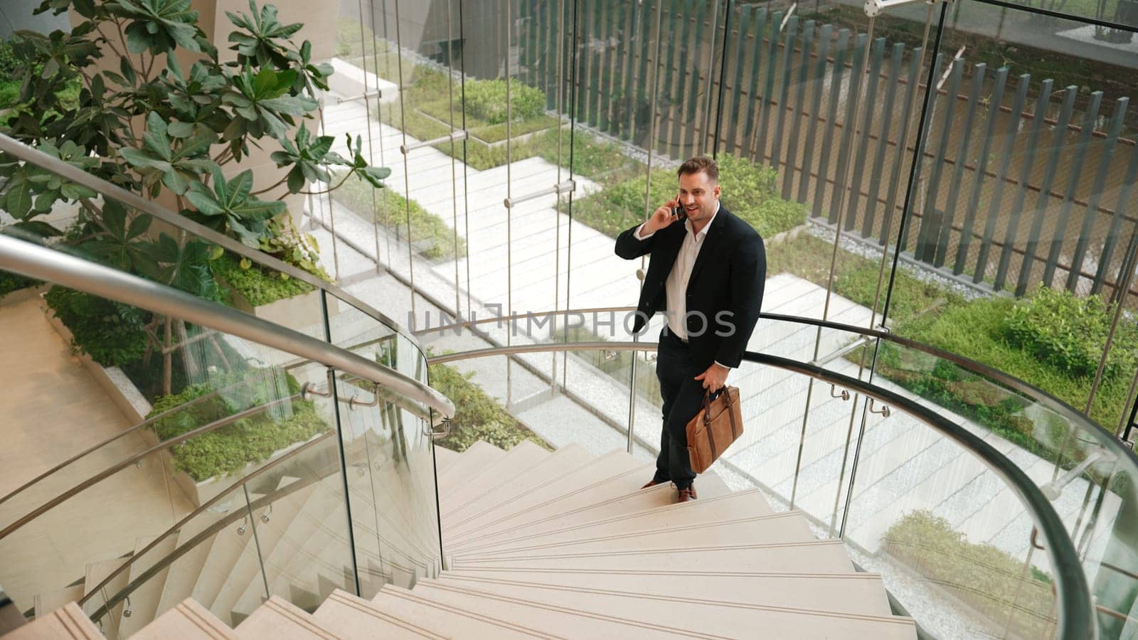 Caucasian businessman calling manager by using smart phone and discuss about financial report. Male leader talking marketing team by using telephone while standing at stair in modern building. Urbane.