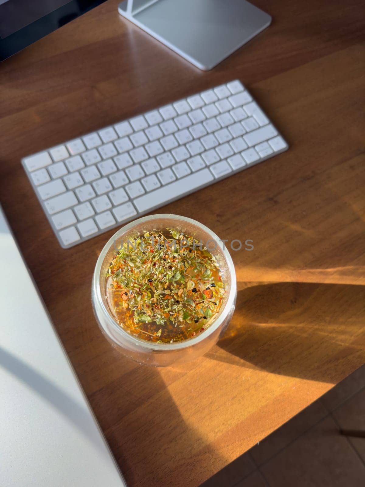 herbal tea with fruits is brewed in a transparent glass cup on the table, sunlight through the window beautifully illuminates the tea, a desktop with a laptop, monitor, wireless keyboard. High quality photo