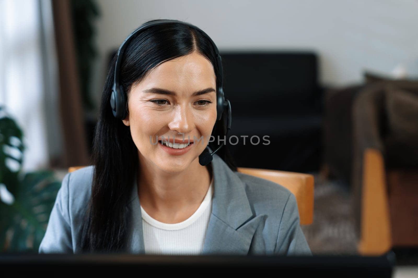 Female call center operator or customer service helpdesk staff working on workspace while talking on the headset to provide assistance for customer. Professional modern business service. Blithe