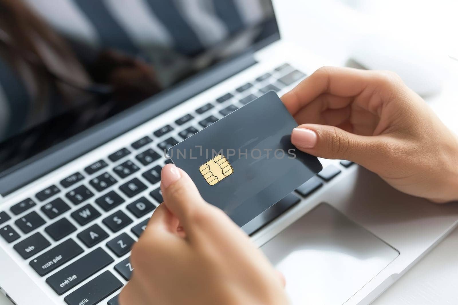 Close up of a woman's hands holding a gray credit card in front of a laptop computer by nijieimu