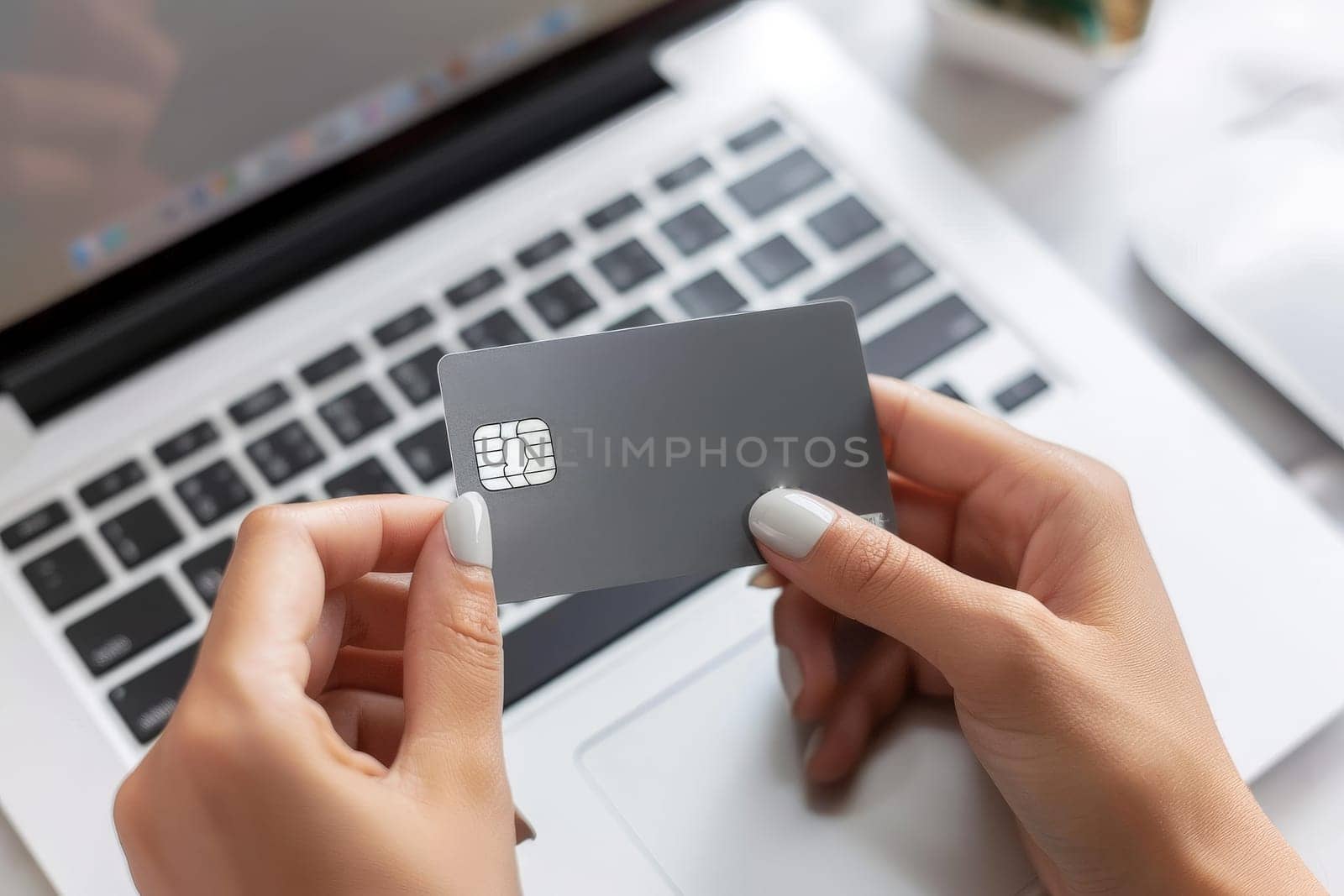 Close up of a woman's hands holding a gray credit card in front of a laptop computer.
