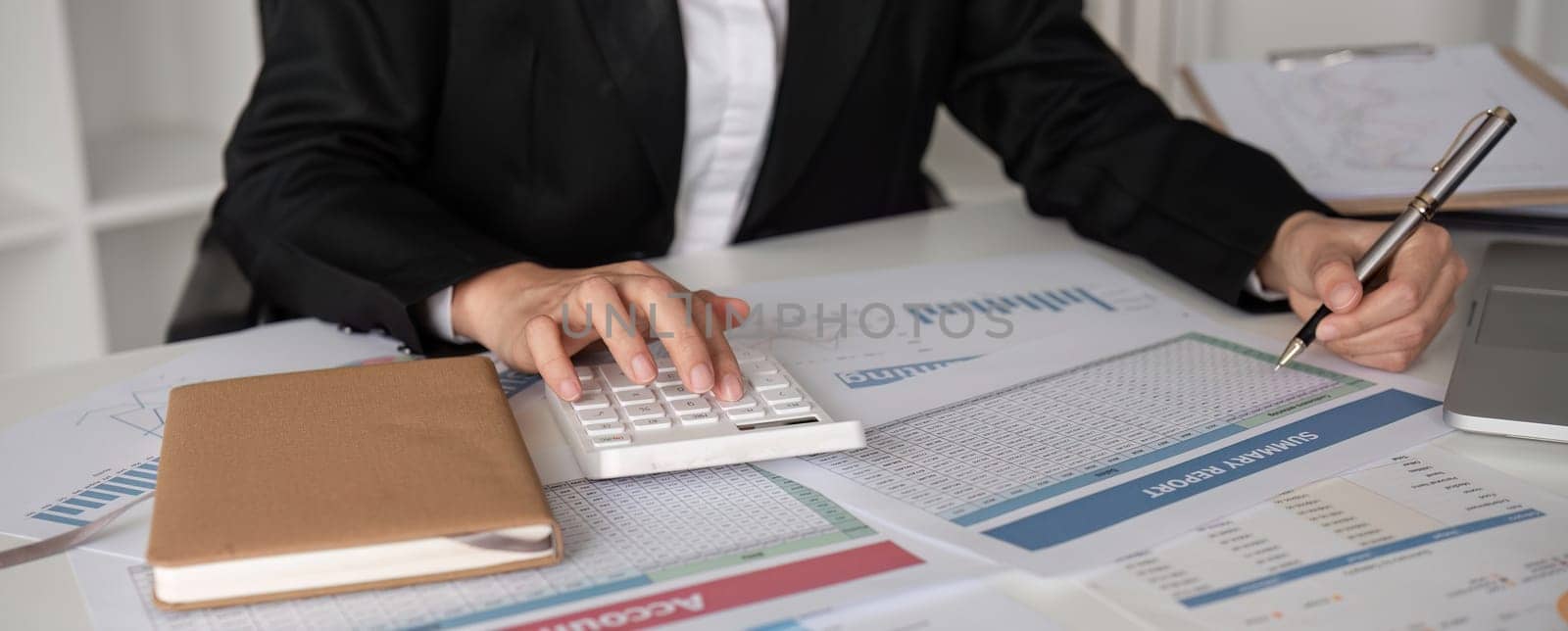 Close up, A young accountant calculates financial figures and company spending graphs using a calculator and laptop to take notes..