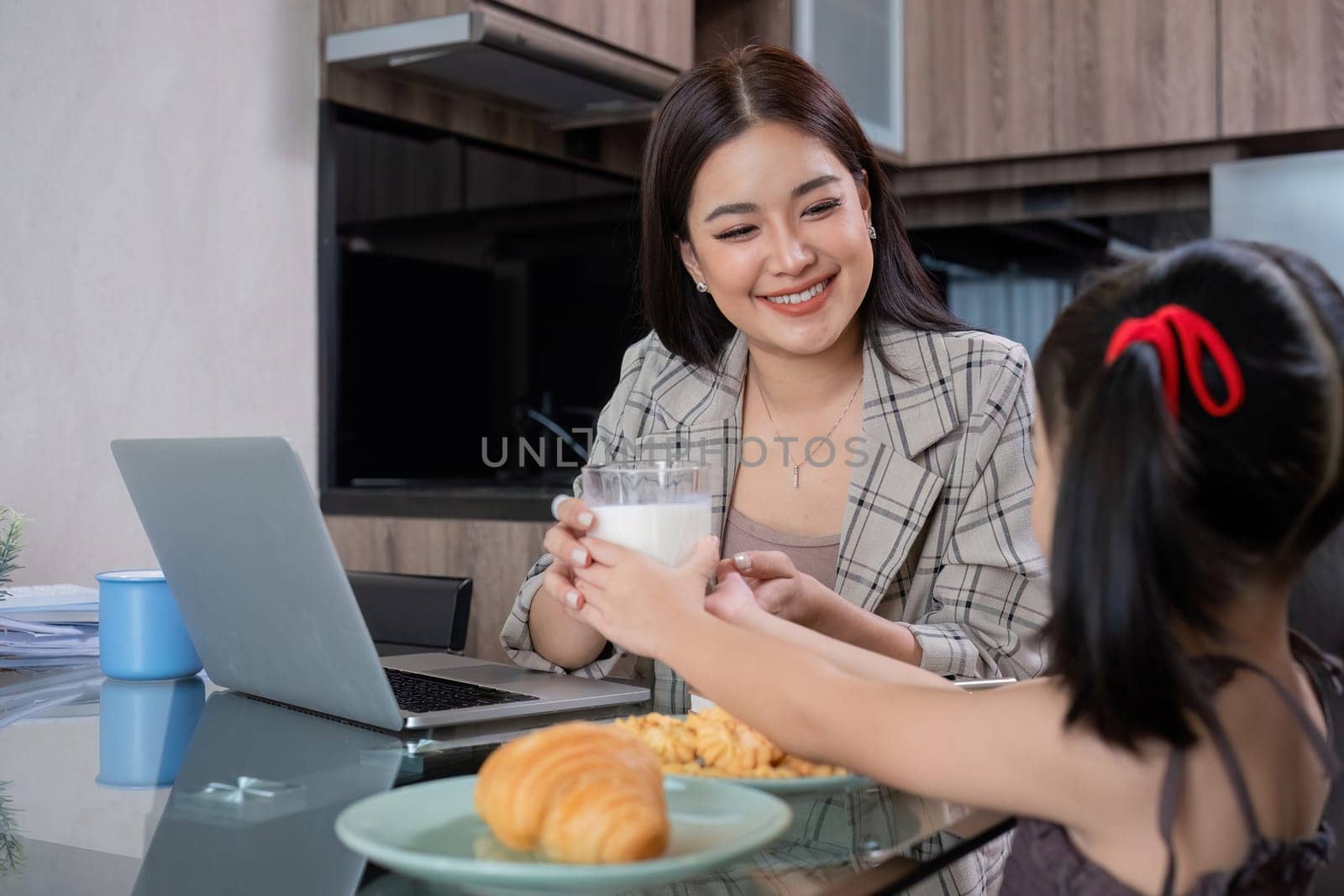 A young single mother receives a snack and eats it with her daughter while she works at home on her laptop..