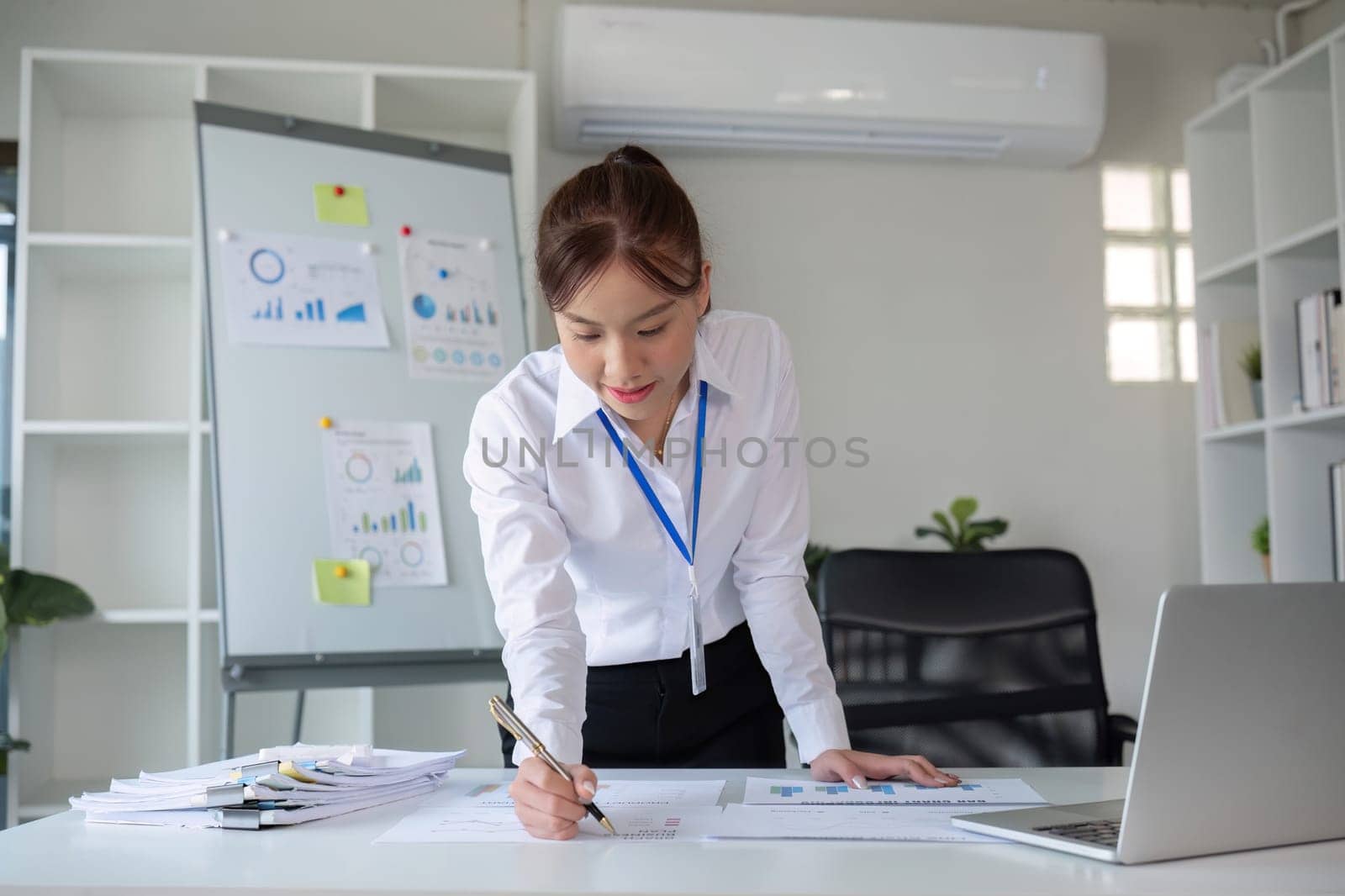 A businesswoman with determination takes note, write work plan and graphs the company's financial schedule in her office..