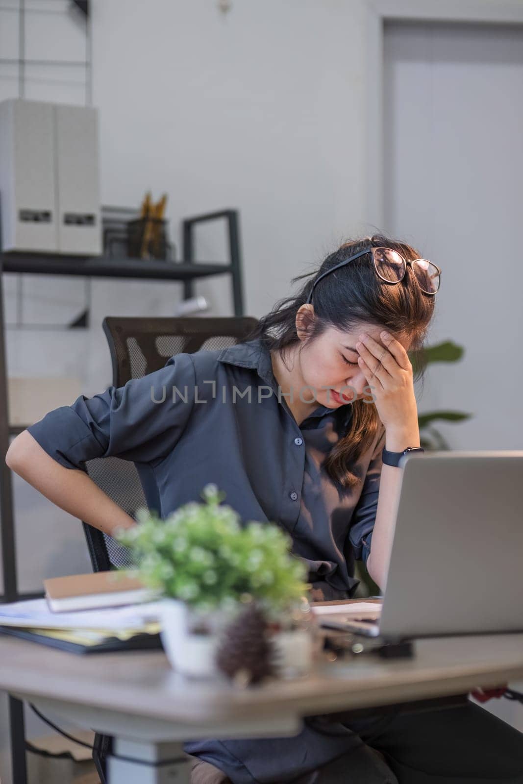 Asian businesswoman feeling tired and stressed over an unsuccessful business while working in a home office decorated with soothing green plants. by wichayada
