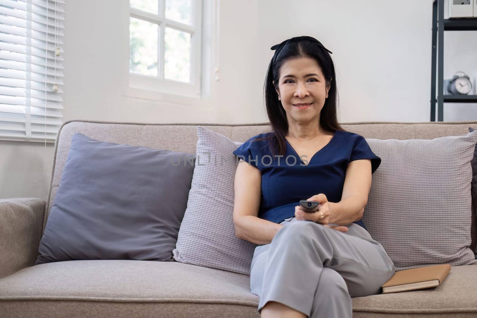 Elderly woman's leisure day watching TV, relaxing on the sofa in the living room..