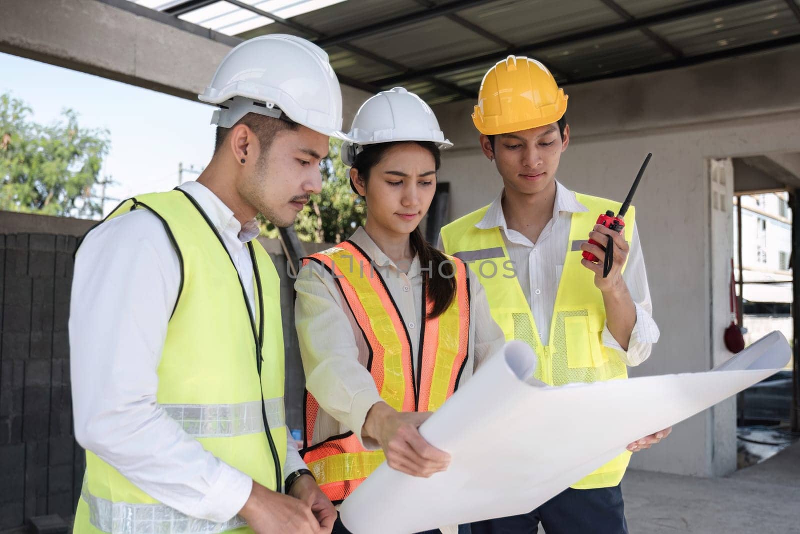 team of civil engineers and architects wearing hard hats Currently in a brainstorming meeting holding project plans to plan a building construction project. by wichayada