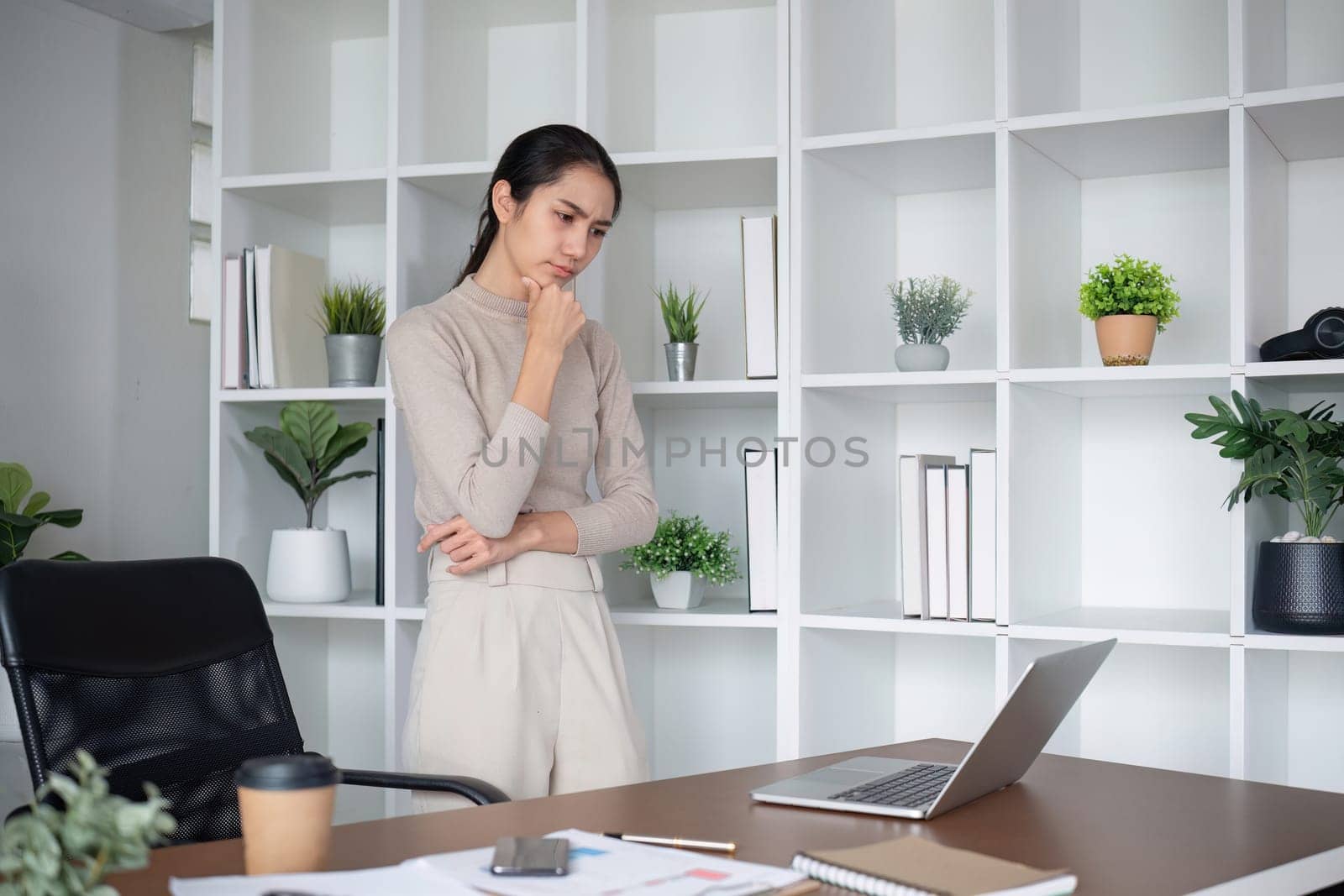 Asian businesswoman feeling tired and stressed over an unsuccessful business while working in a home office decorated with soothing green plants..