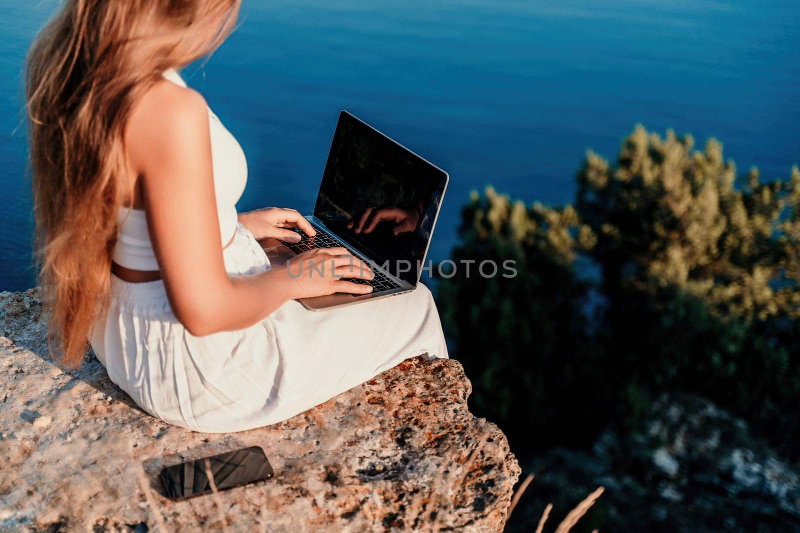 Freelance women sea working on the computer. Good looking middle aged woman typing on a laptop keyboard outdoors with a beautiful sea view. The concept of remote work