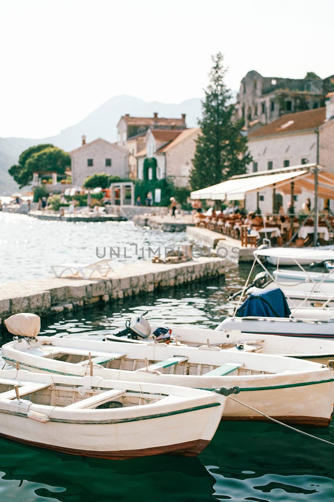 White wooden fishing boats are moored at the pier. Perast, Montenegro by Nadtochiy