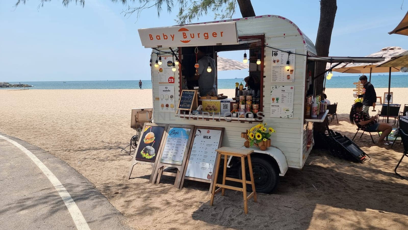 A vibrant food truck is parked on the sandy shore of a beach, serving up delicious dishes to beachgoers under a clear blue sky by fokkebok