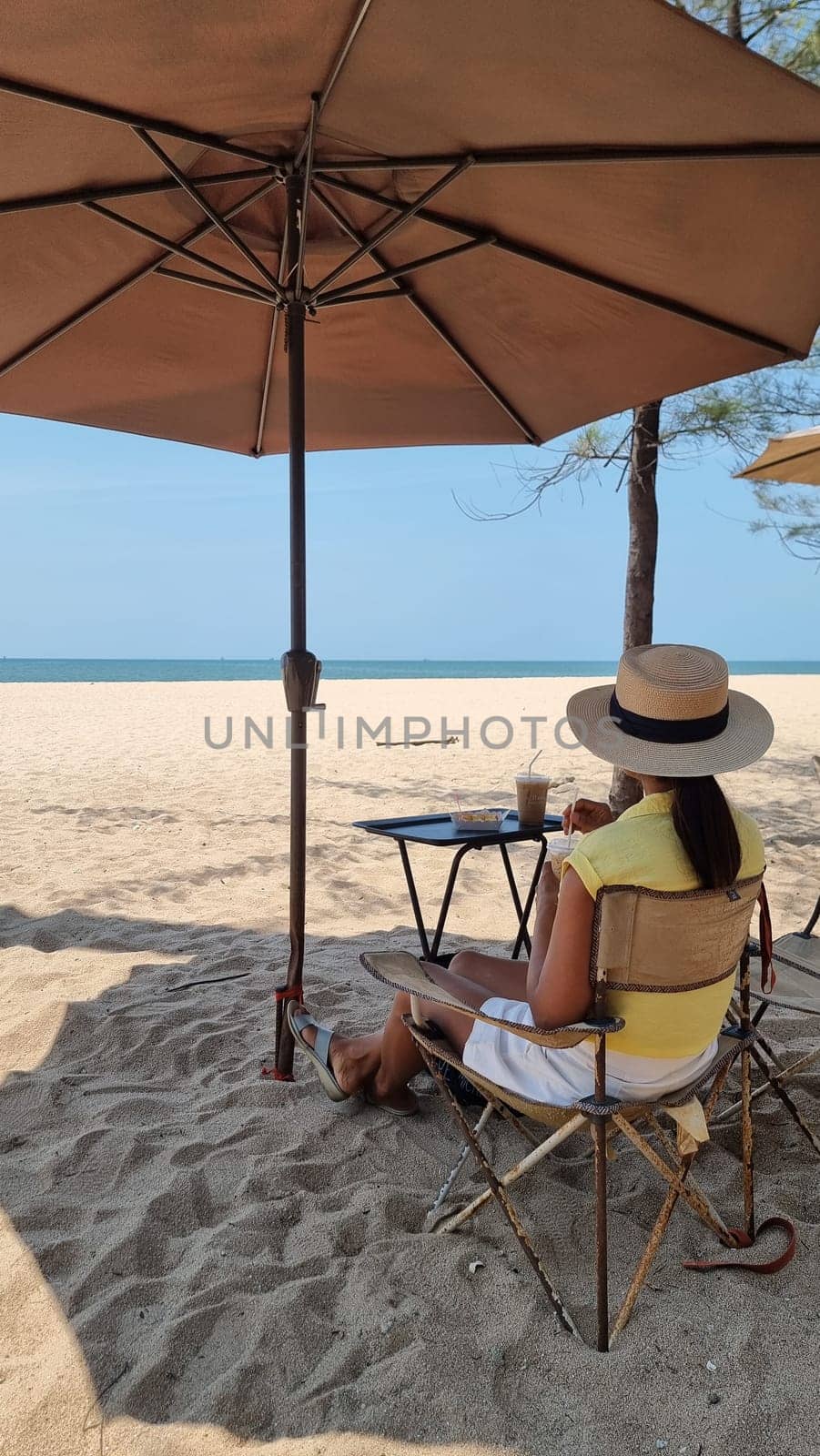 A woman relaxes in a chair under an umbrella on the sandy beach, enjoying the peaceful ambiance of the ocean waves by fokkebok